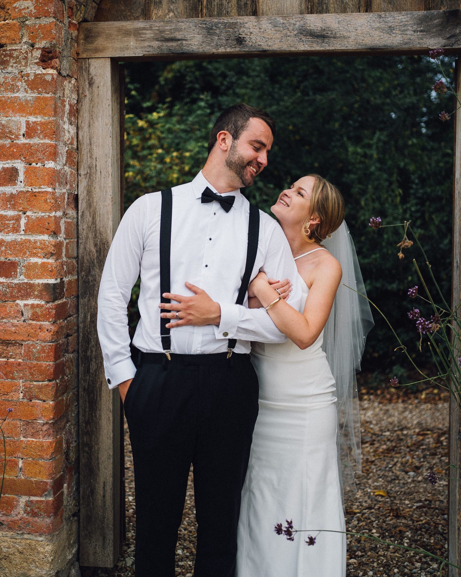 Candid wedding portraits showing natural laughter against rustic brick backdrop.