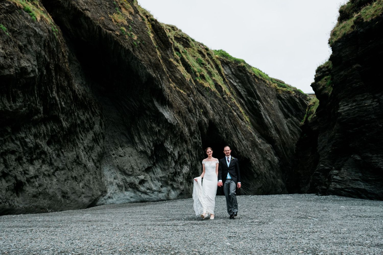 Scenic beach wedding photos with dramatic black cliffs and overcast sky.