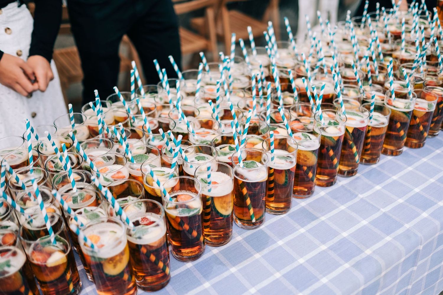 Long row of signature cocktails with blue straws lined up on wedding reception bar.