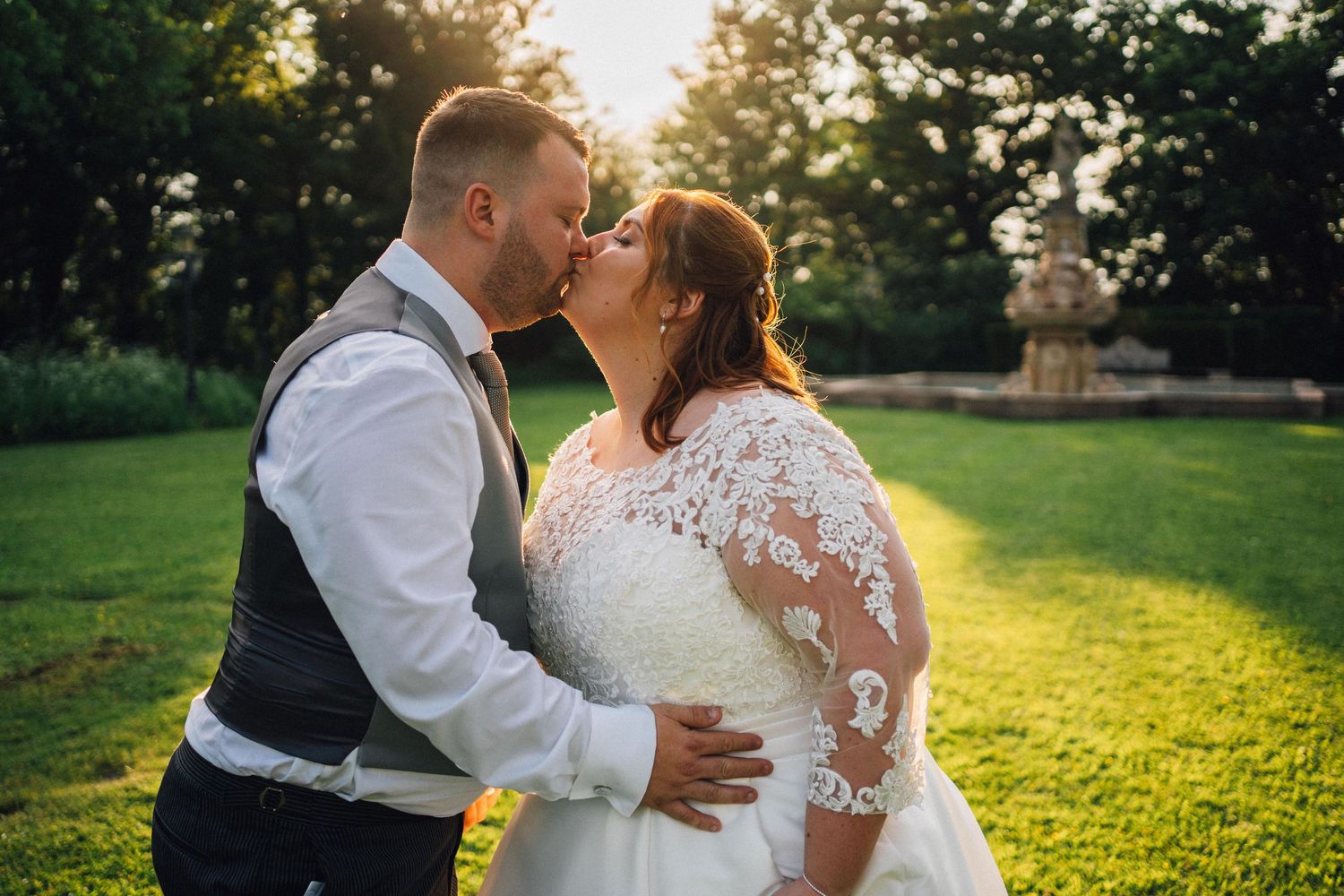 A romantic sunset wedding photoshoot in a lush green field with golden light streaming through the trees.