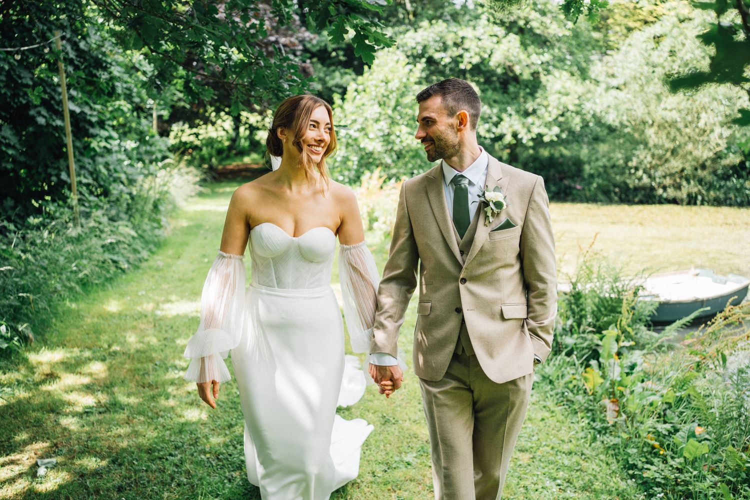 A couple walks together outdoors on their wedding day through a lush garden setting.