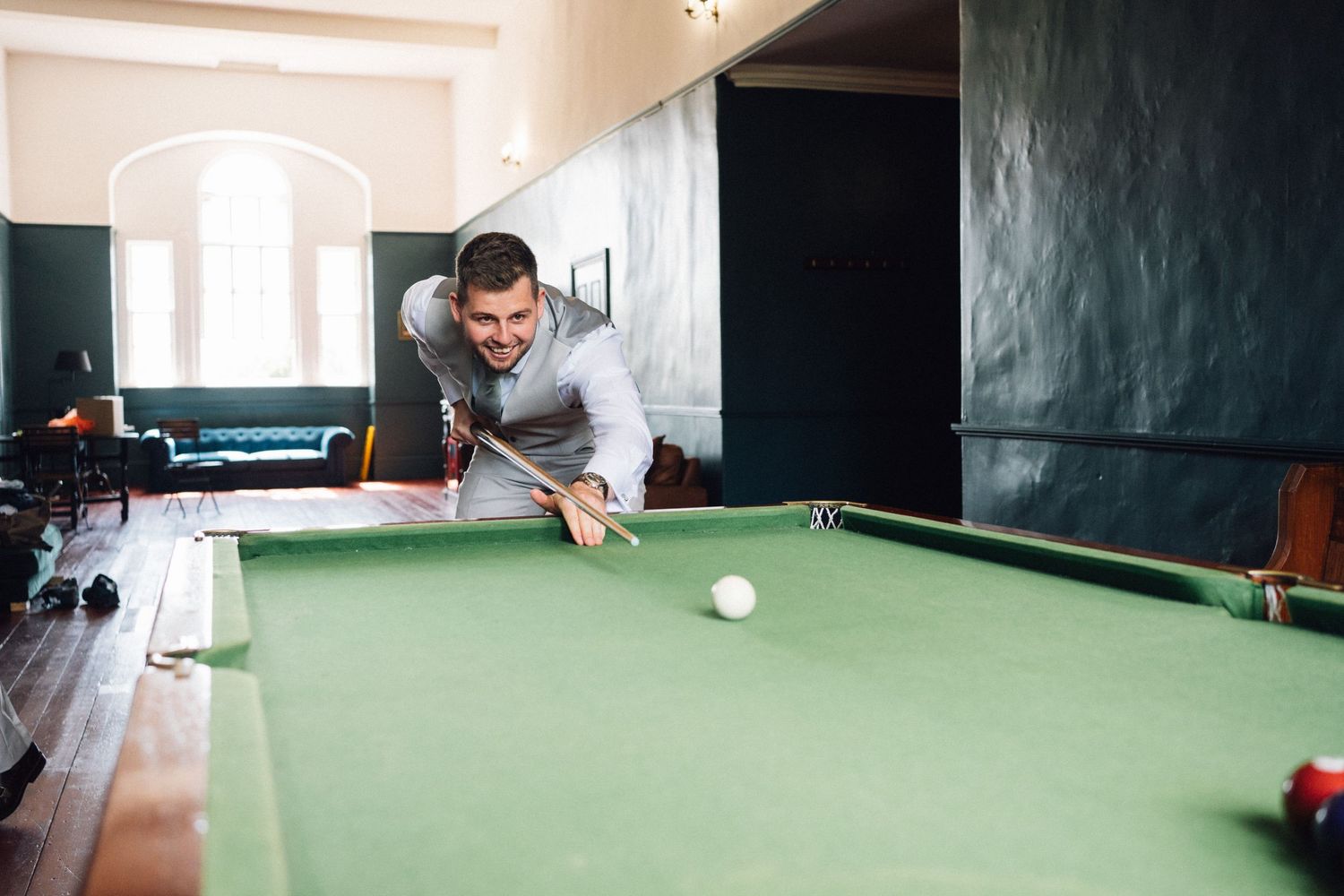 A person in casual attire leans over a green pool table preparing to take a shot.