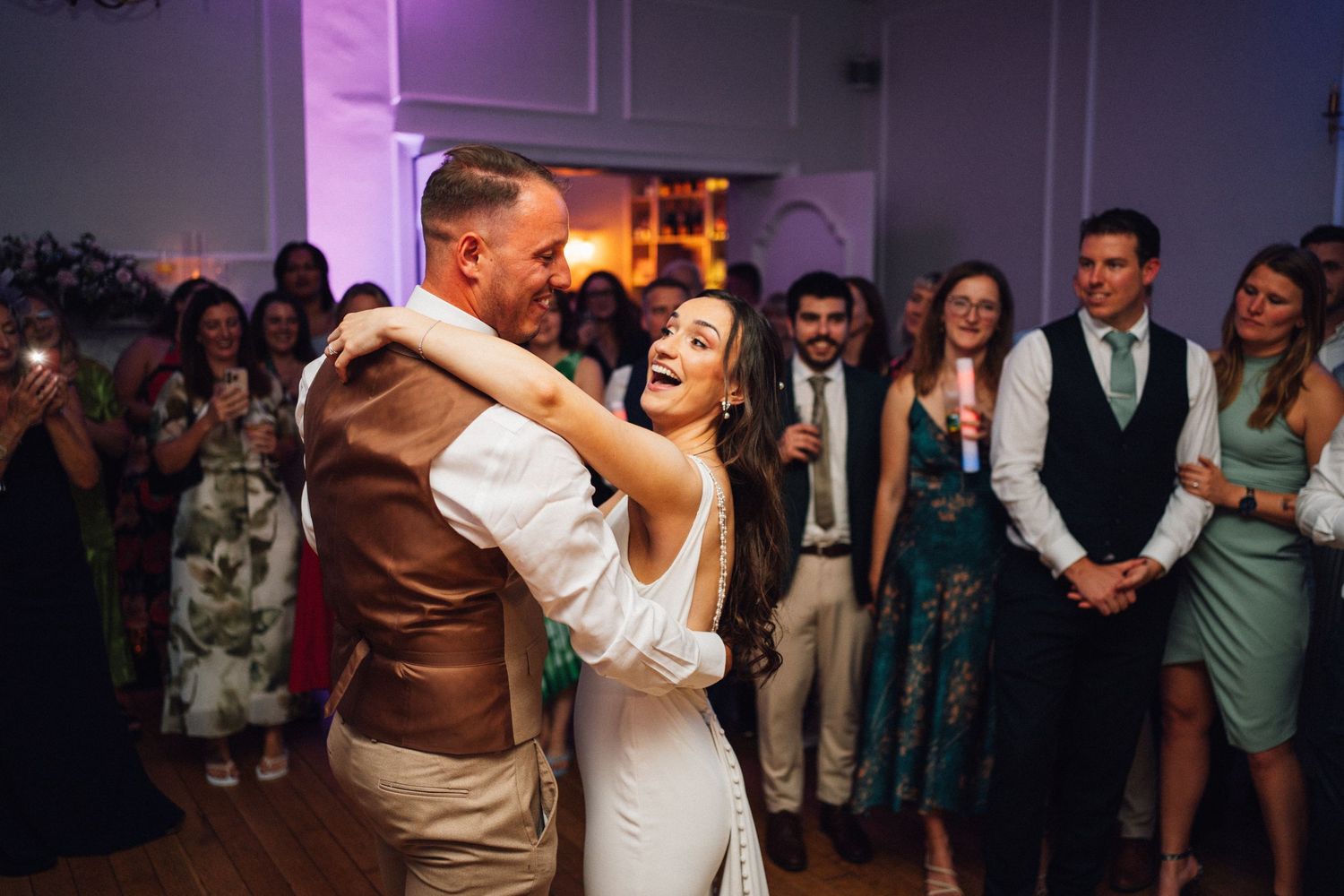 Wedding reception dance floor filled with guests dancing under purple lighting.
