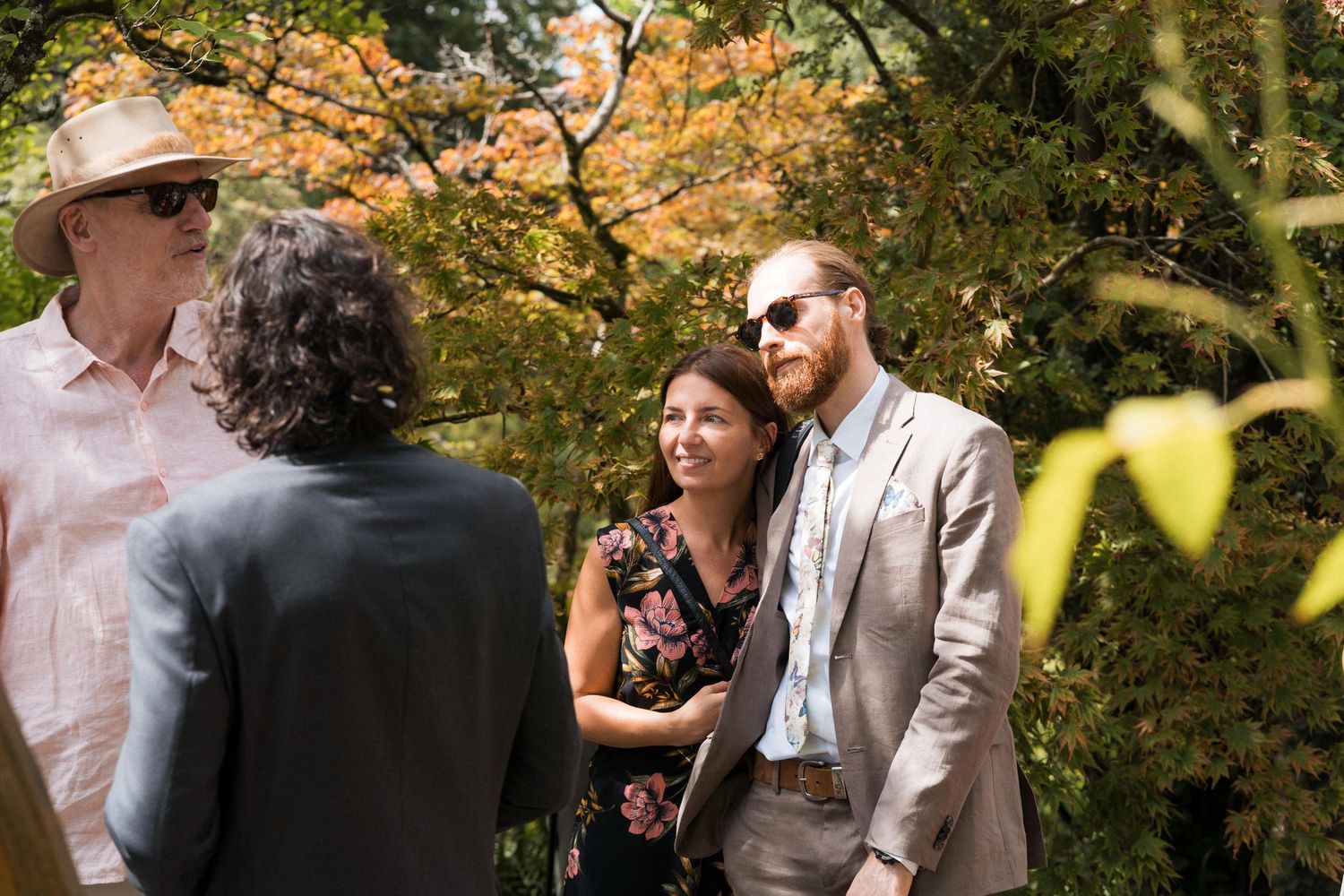 Couple smiling outdoors at a garden wedding ceremony surrounded by autumn foliage and guests.