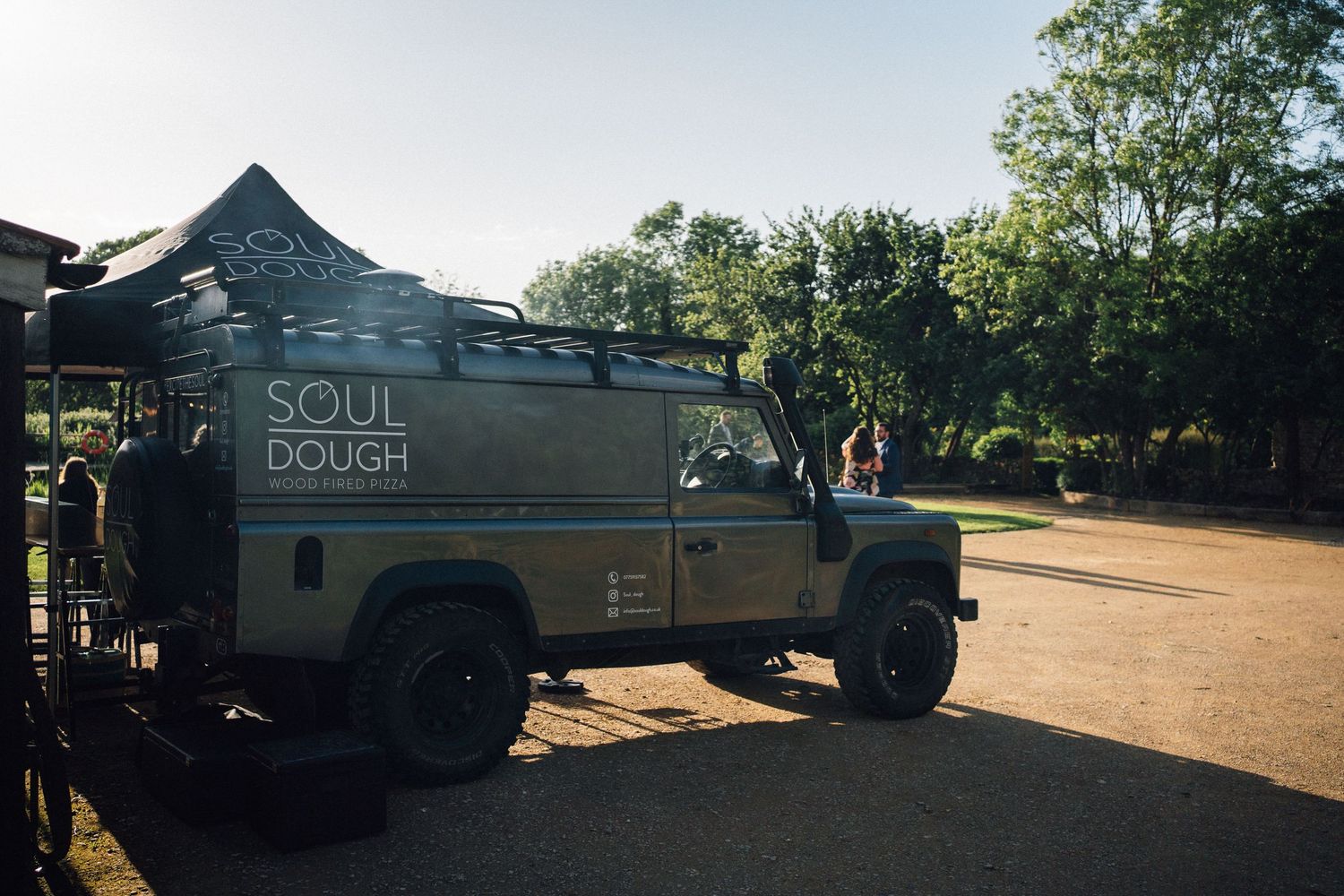 Food trucks and catering vehicles parked outside a rustic wedding venue on a sunny day.