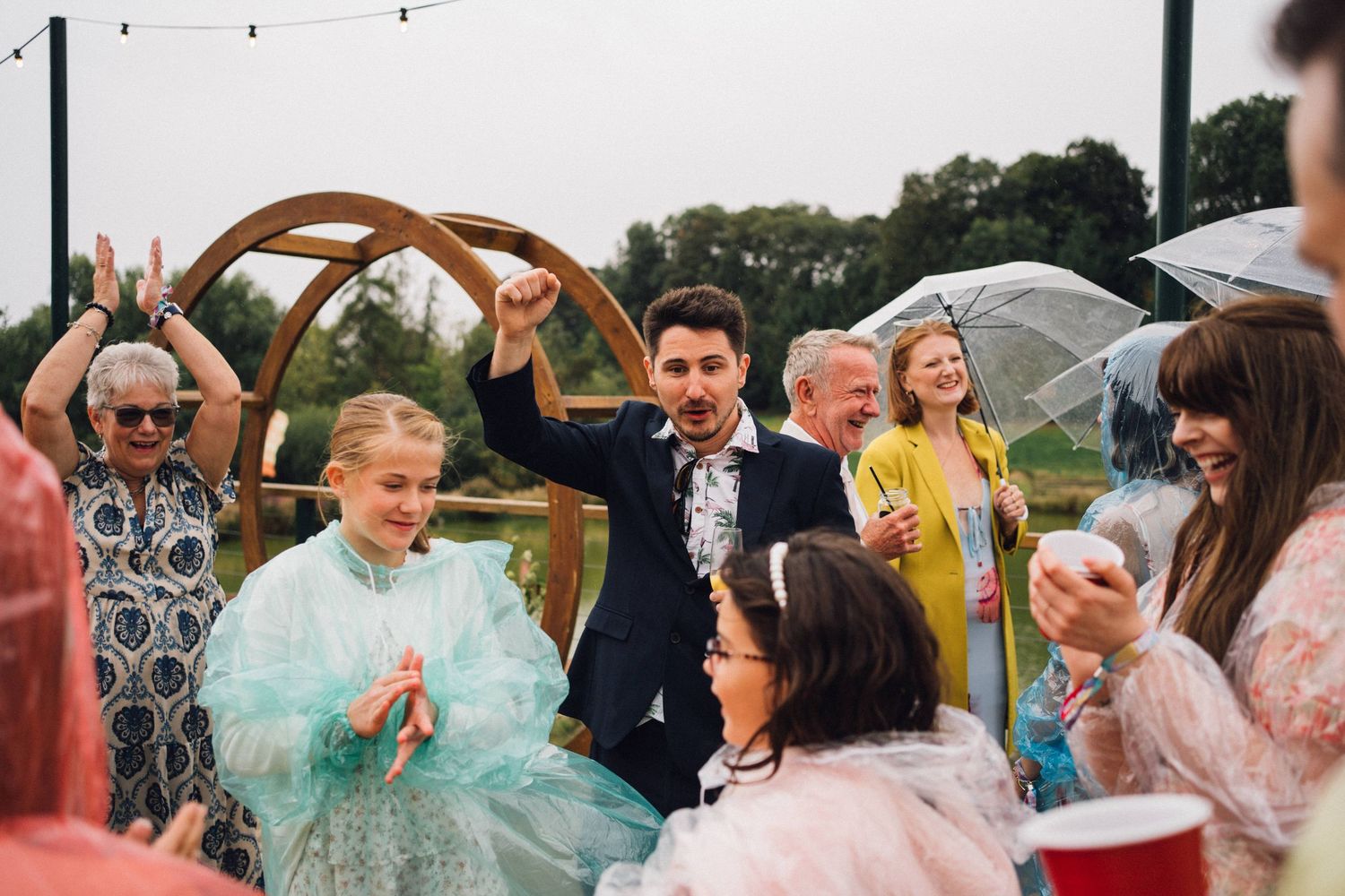 Guests in rain ponchos enjoying an outdoor celebration with string lights overhead.