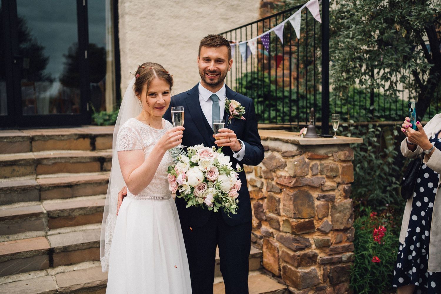 Wedding party stands in front of a rustic stone wall with bunting decorations.