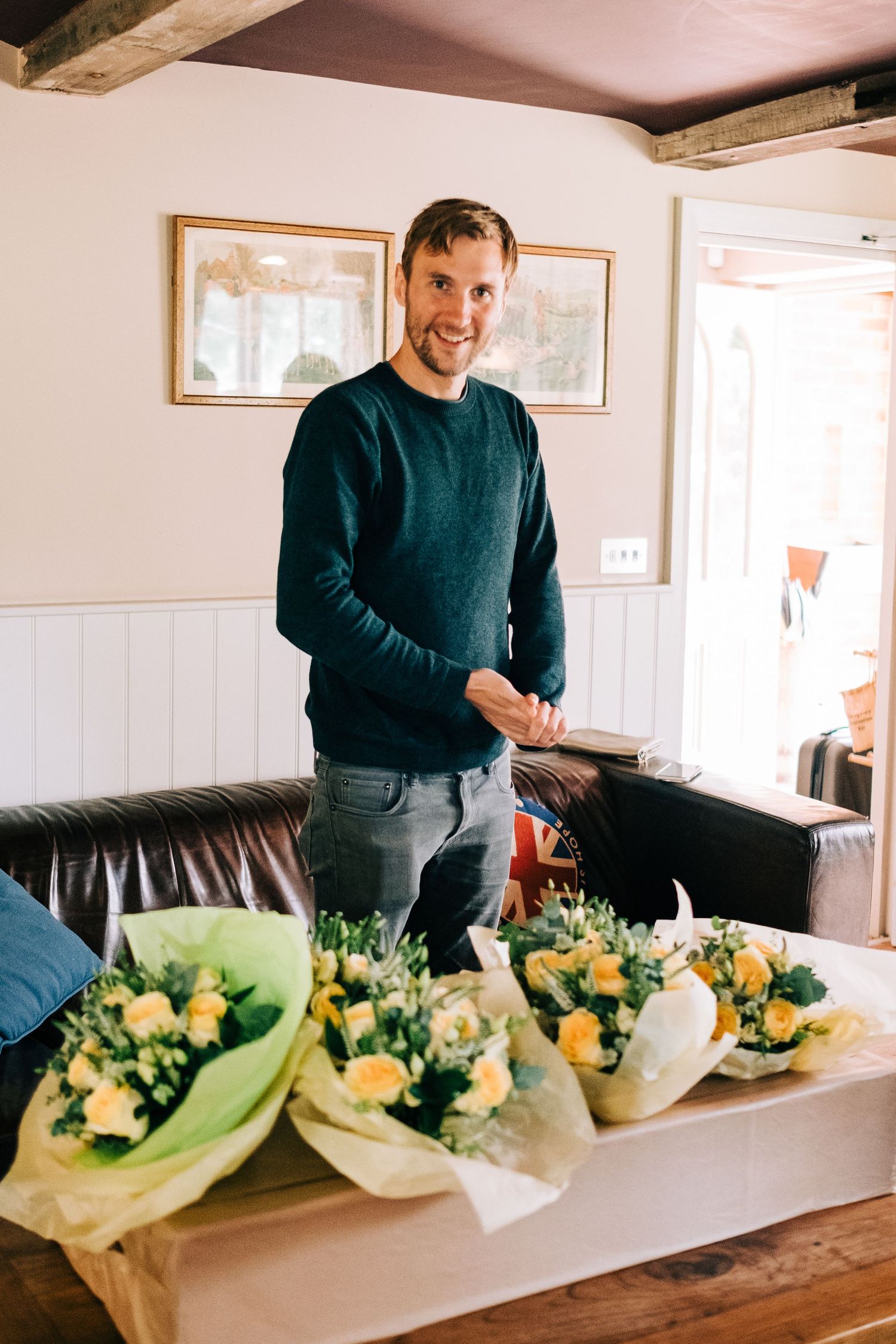 Person in navy sweater arranging yellow floral bouquets on wooden table.