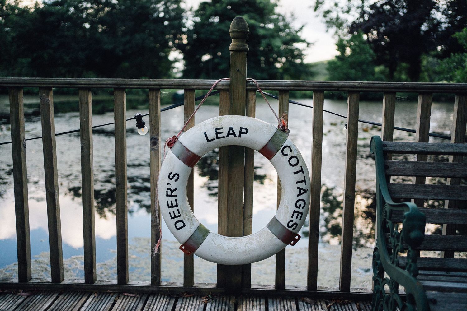 Life preservers hang on a wooden dock railing overlooking a serene lake at sunset.