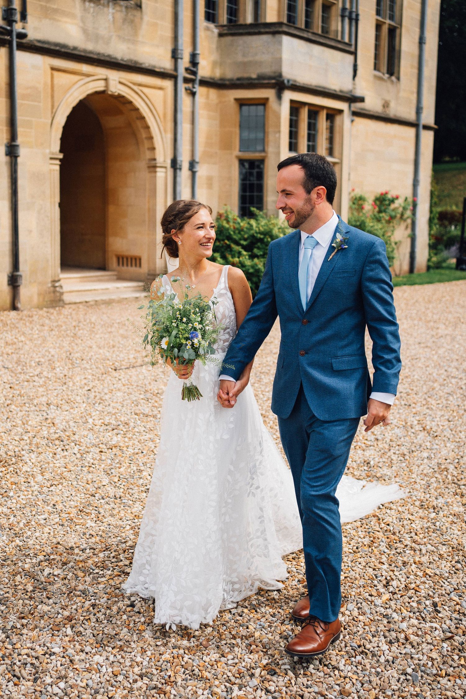 Couple walking together on a gravel path outside a grand stone building.