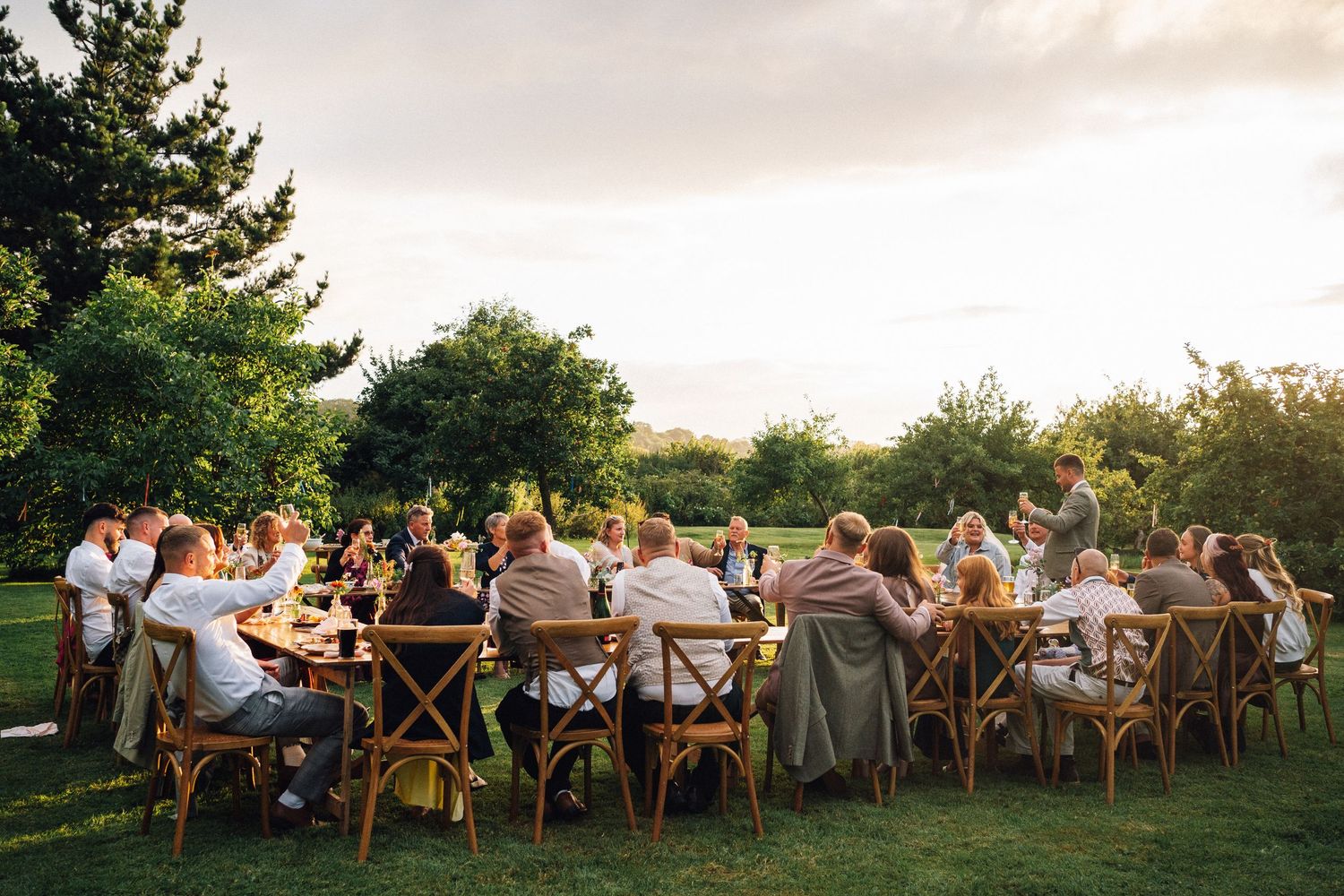 Wedding guests seated at long tables in an outdoor garden setting during golden hour.