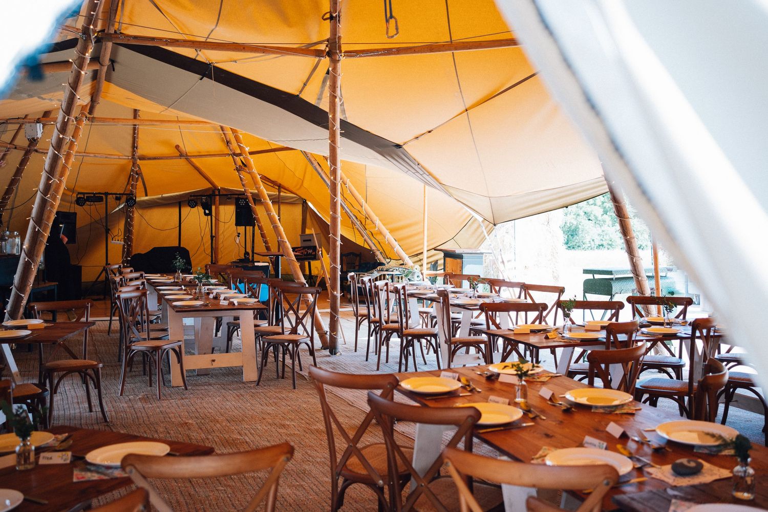 Interior view of a large canvas tent event space with wooden tables and chairs set up for dining.