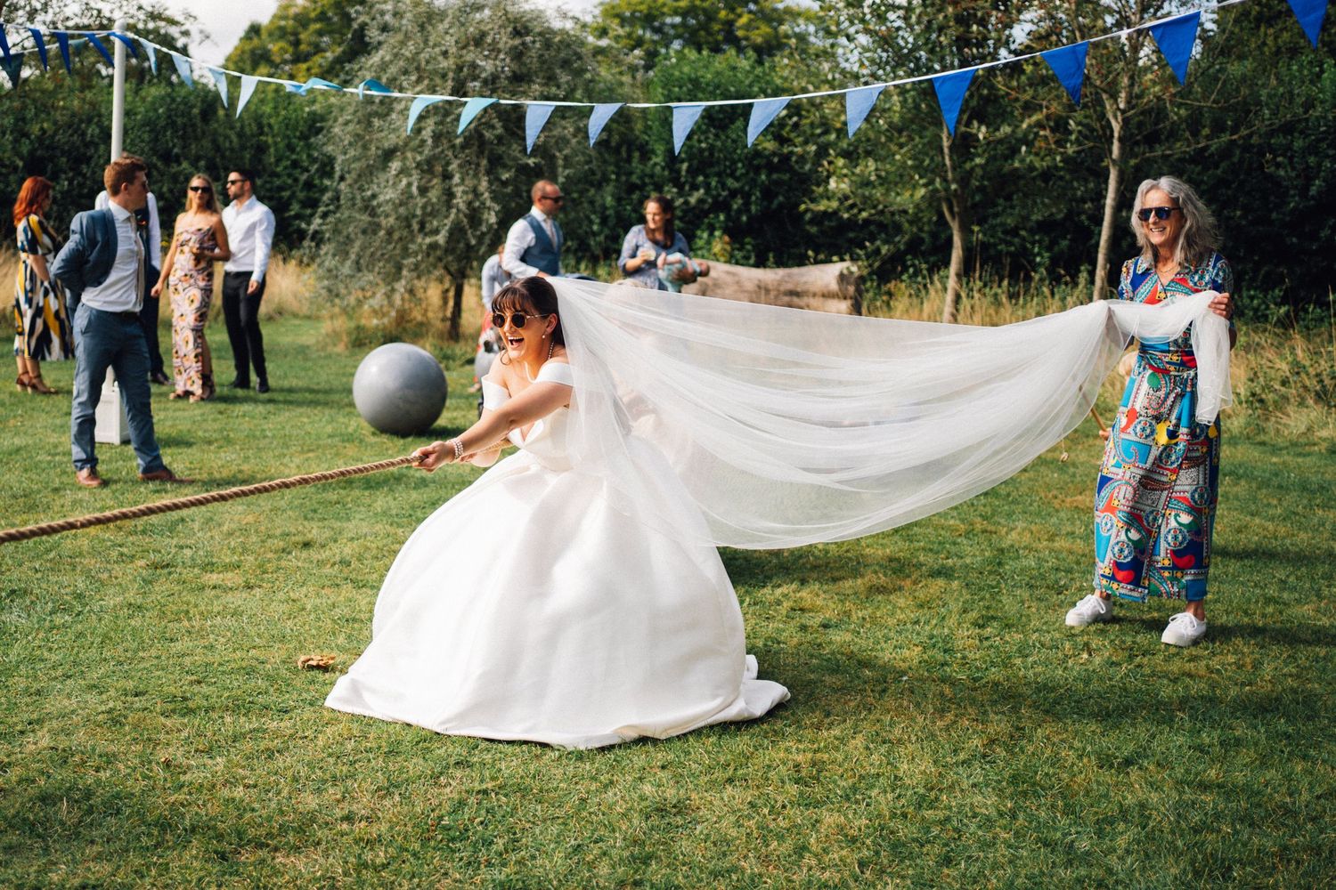 Flowing white wedding dress veil blowing in the wind across a sunny green lawn during an outdoor ceremony.