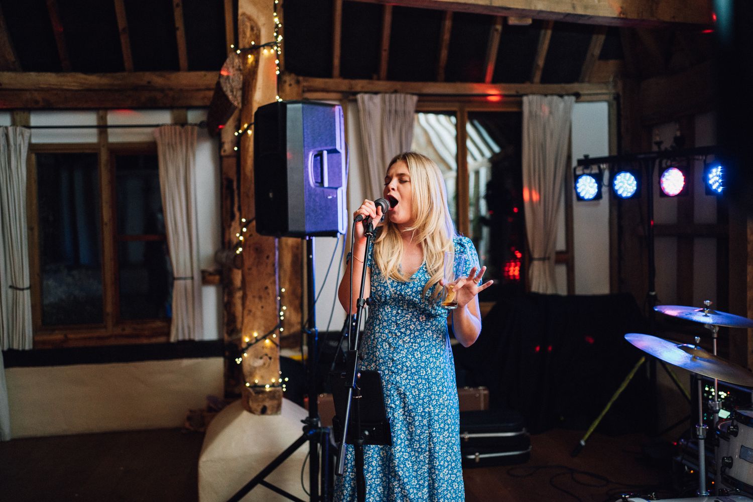 A performer sings into a microphone at a nighttime event with stage lighting in the background.