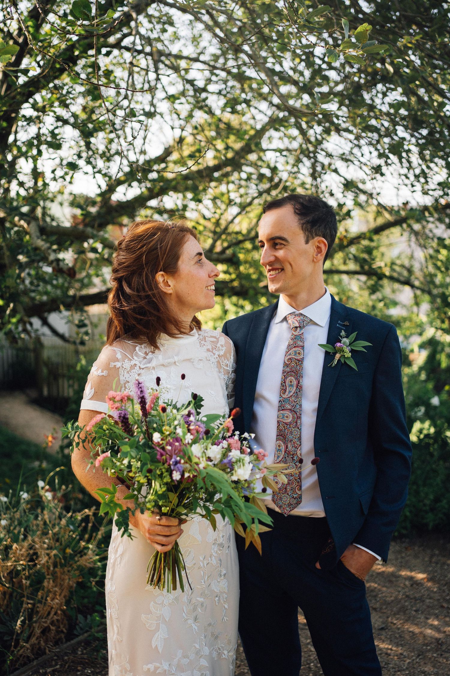 Newlyweds share intimate moments outdoors while bride holds colorful wildflower bouquet.