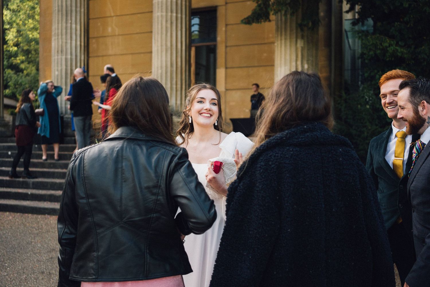 A group of people gather outside a building with classical columns and architecture.