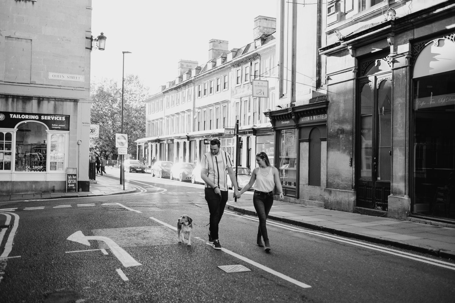 Urban street scene with pedestrians walking past storefronts in black and white photography.
