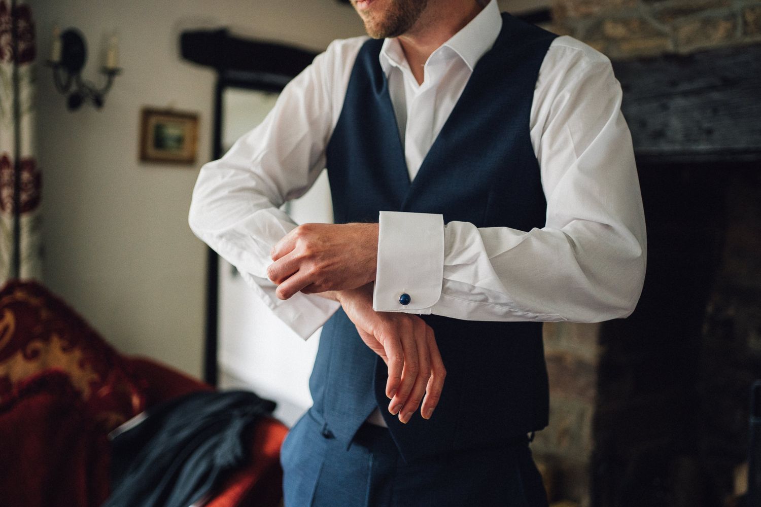 Men adjusting formal wear and buttoning vests during wedding preparations.