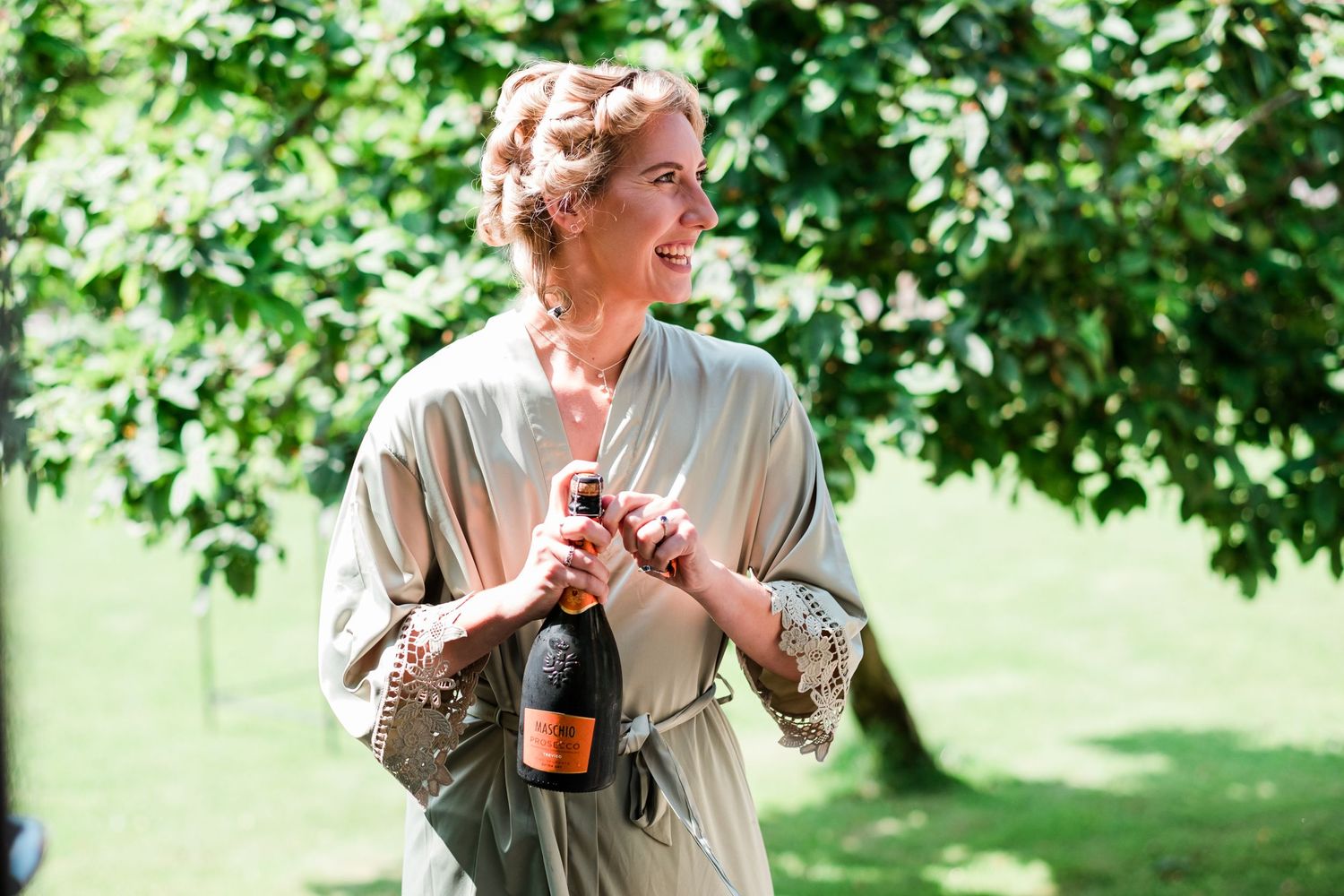 A joyful moment captured outdoors with champagne under green trees on a sunny day.