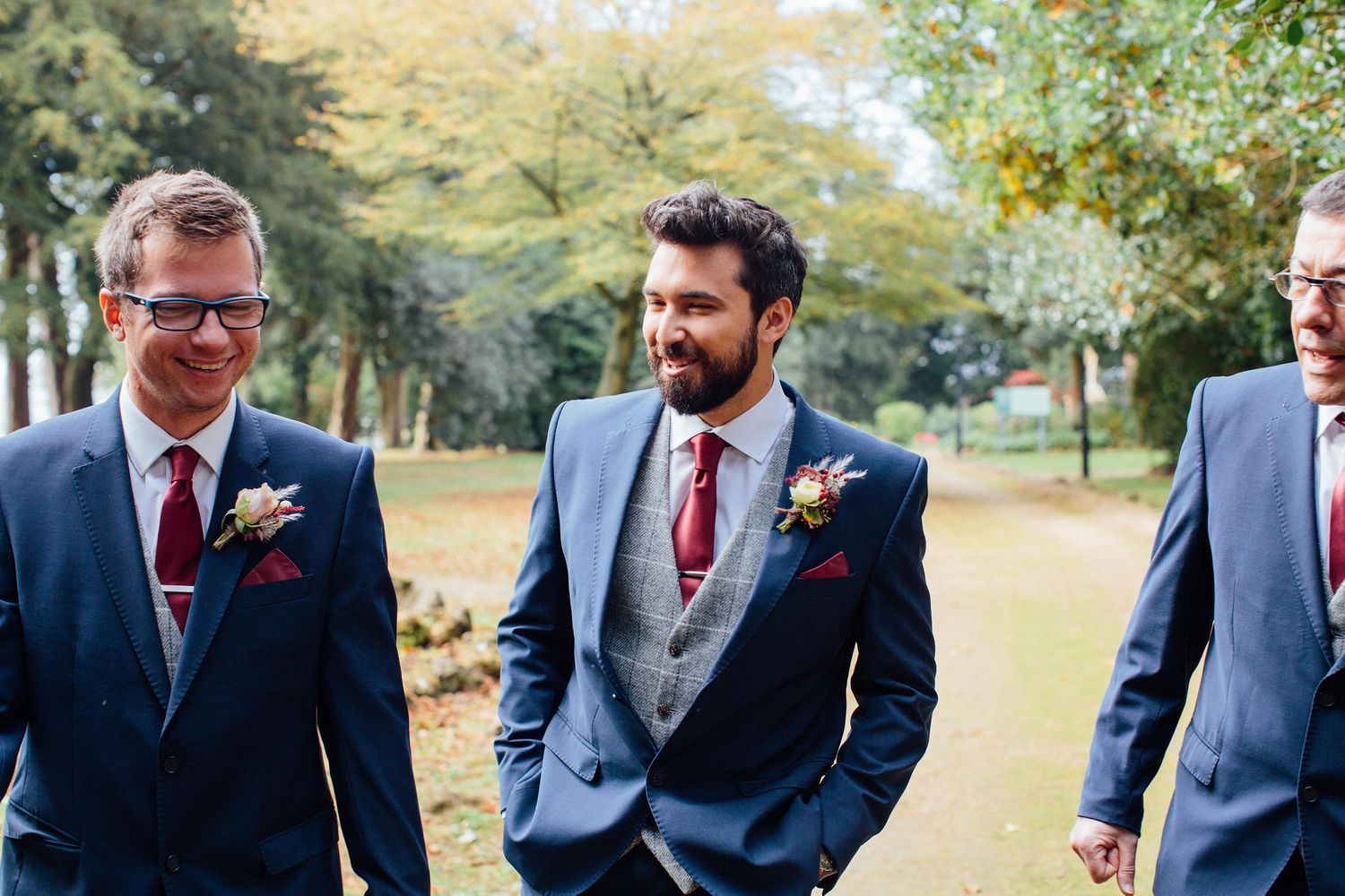 Groomsmen in navy blue suits and red ties standing together outdoors.