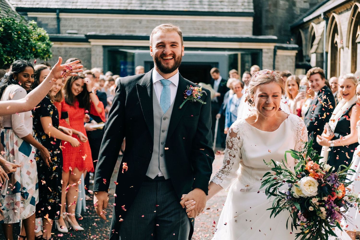 Joyful wedding celebration with guests embracing and laughing outdoors.