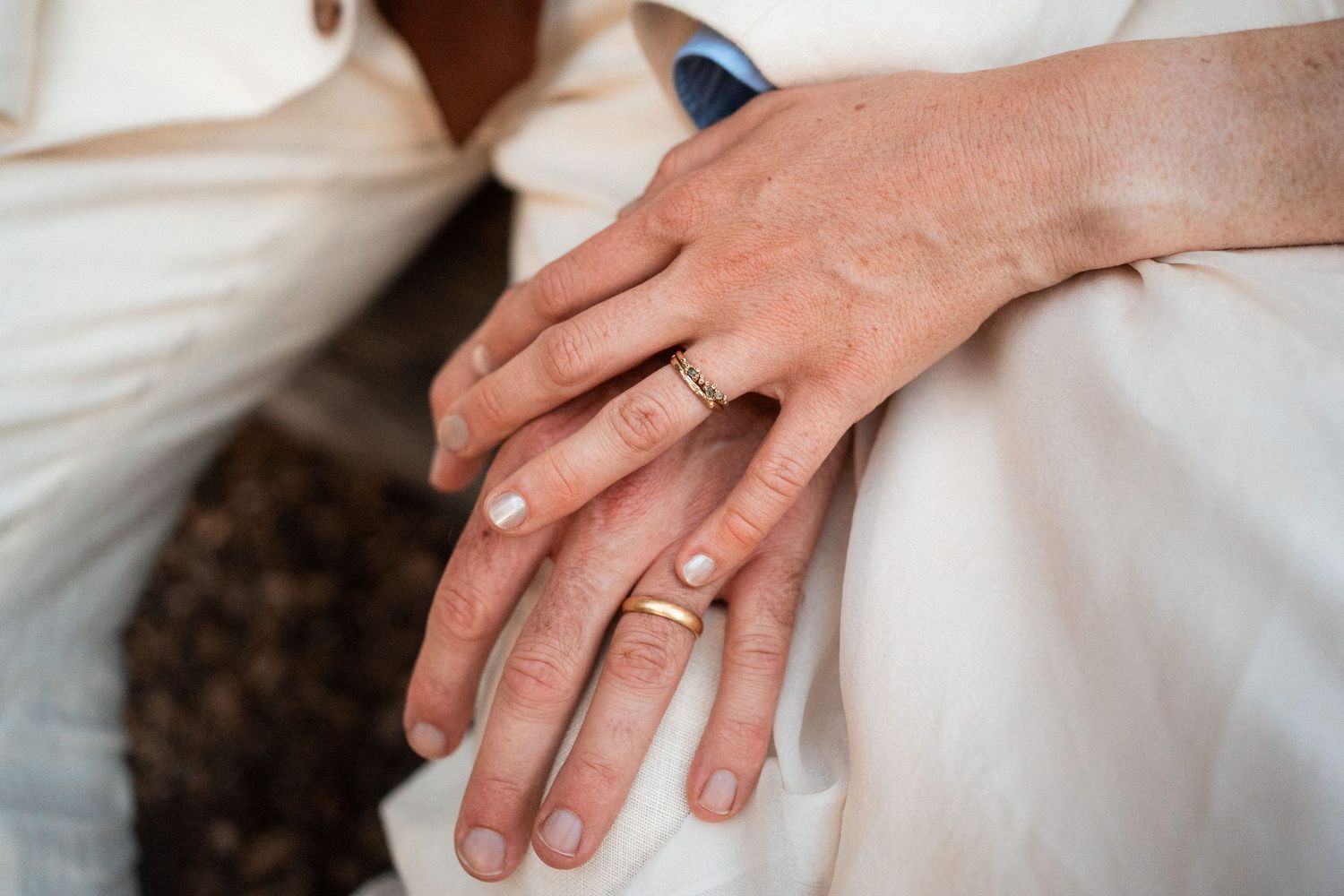 Newlywed couple displays gold wedding rings on clasped hands in elegant white wedding attire.