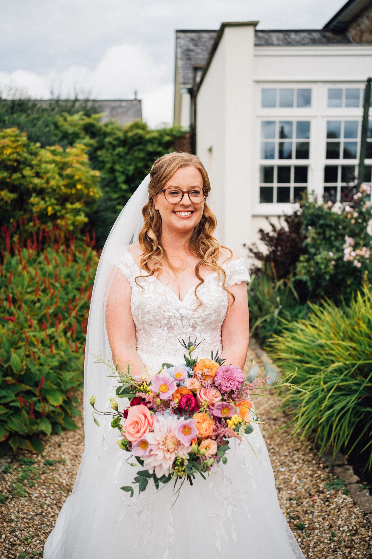 A beautiful bridal portrait series showing a joyful bride in a white lace dress holding a vibrant pink and peach bouquet.