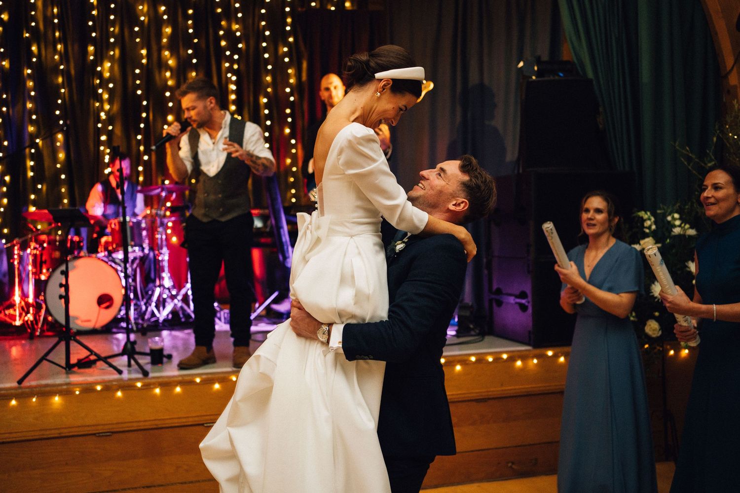 Wedding couple dancing under twinkling string lights at an indoor reception venue.