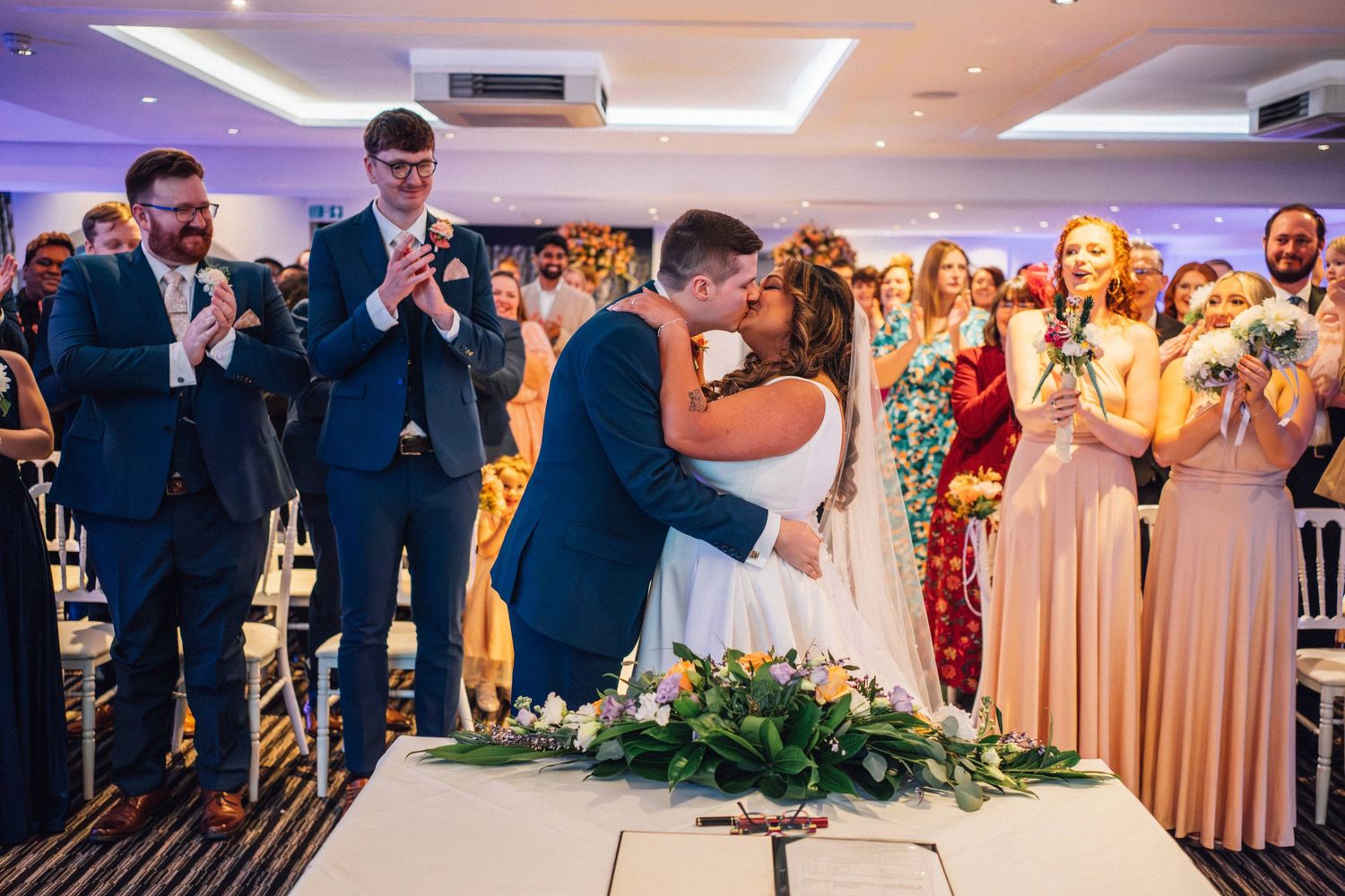 Wedding guests dance and celebrate on an illuminated dance floor during an evening reception celebration.