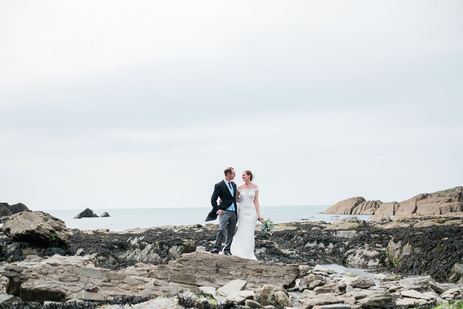 Couple walking along dramatic rocky coastline during wedding photoshoot.