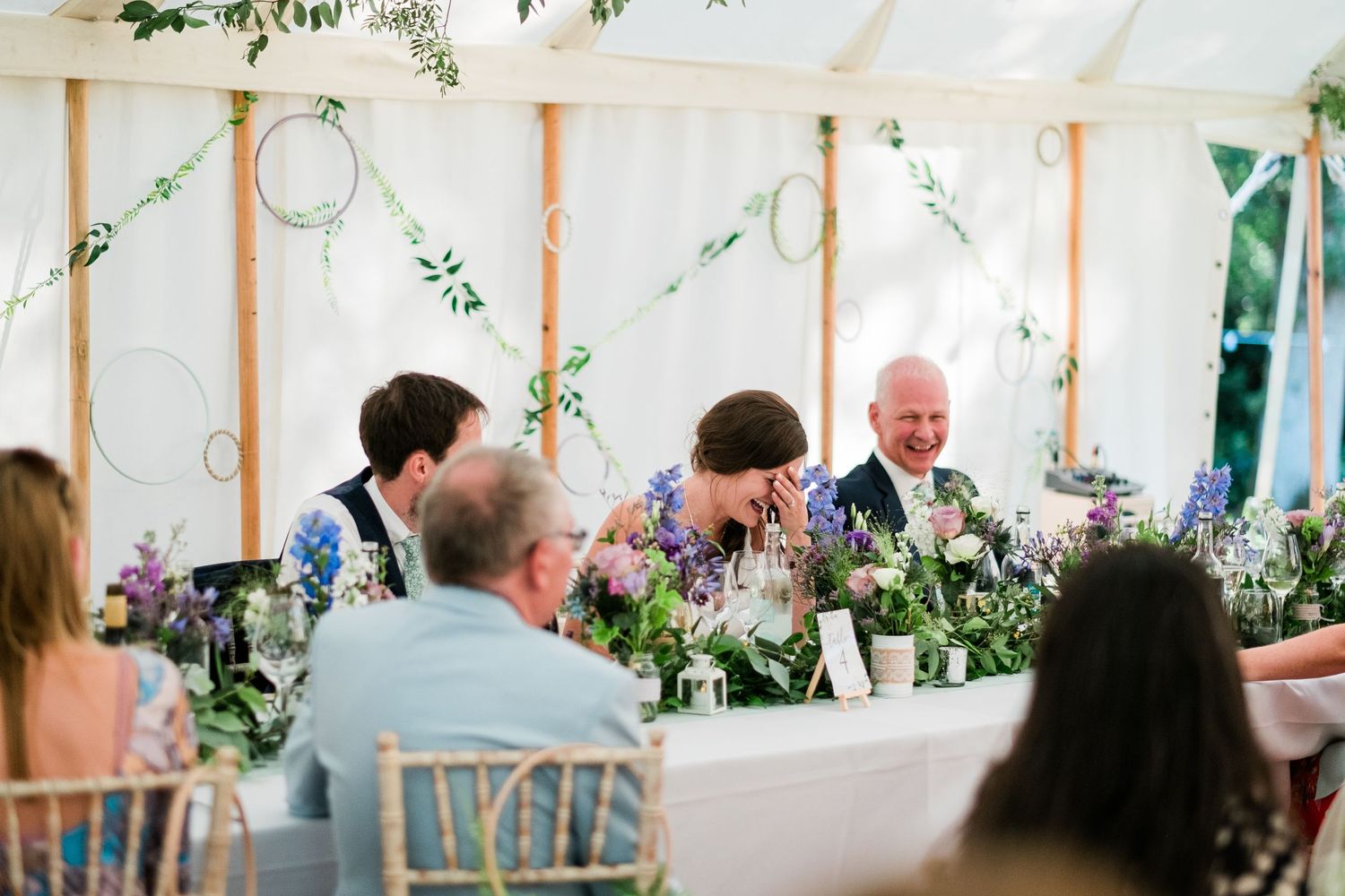 Wedding reception tent decorated with white draping, wooden poles and hanging greenery garlands.