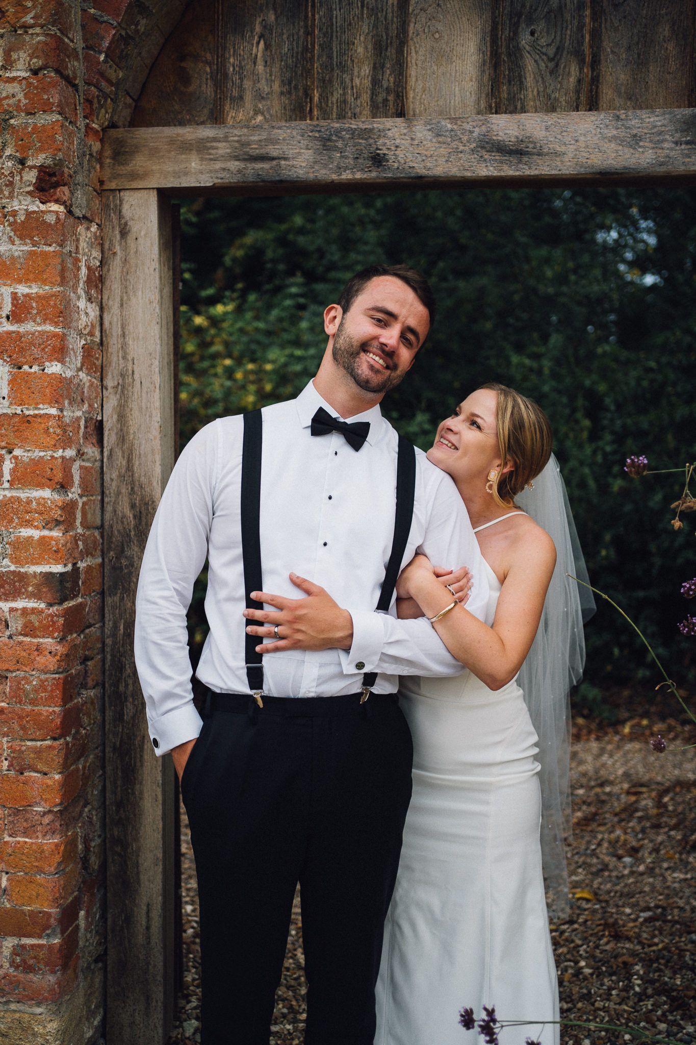 Joyful wedding couple sharing laughs during portrait session against wooden door.