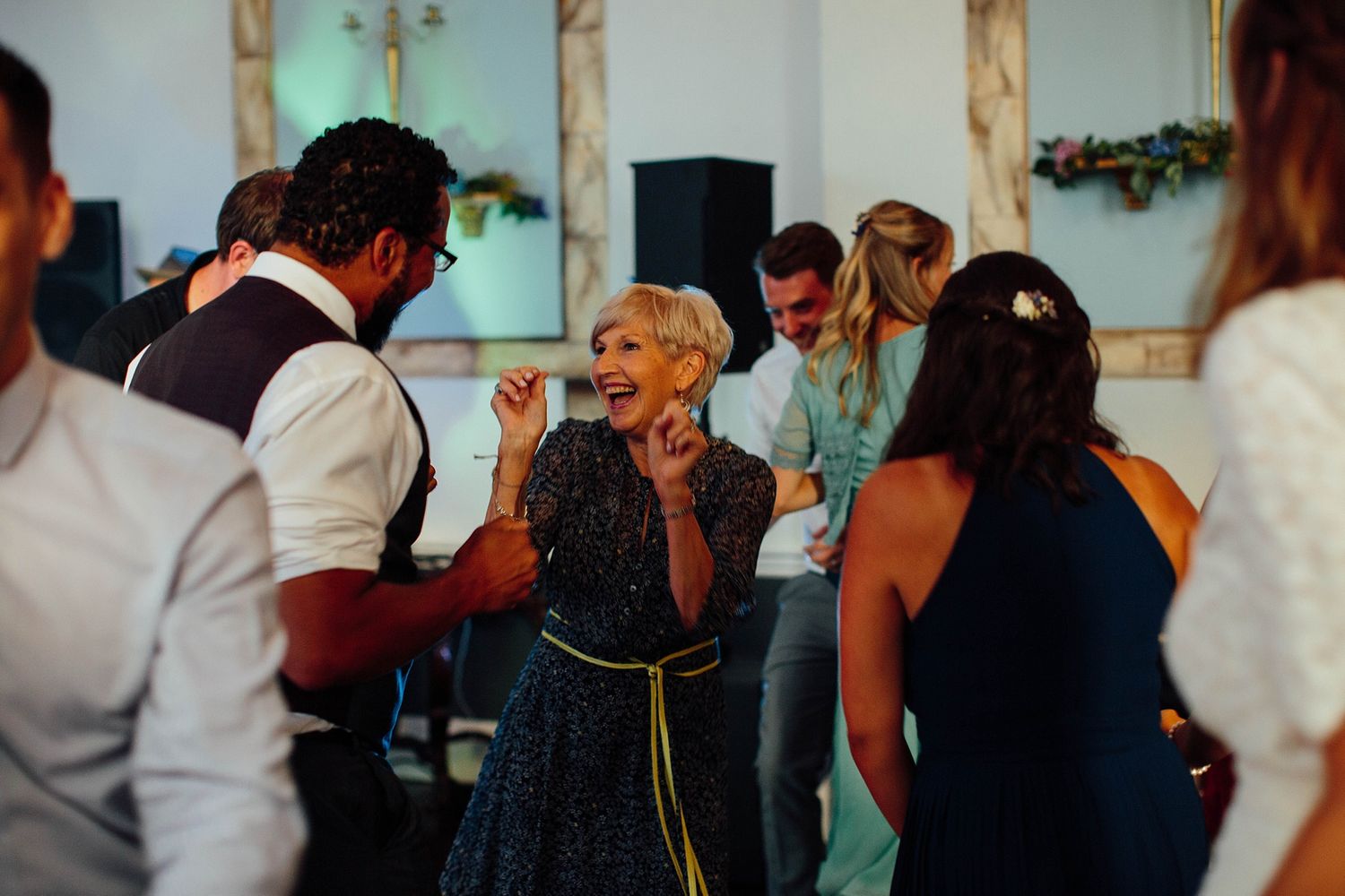 Wedding guests dancing and mingling in an elegant room with wooden columns.