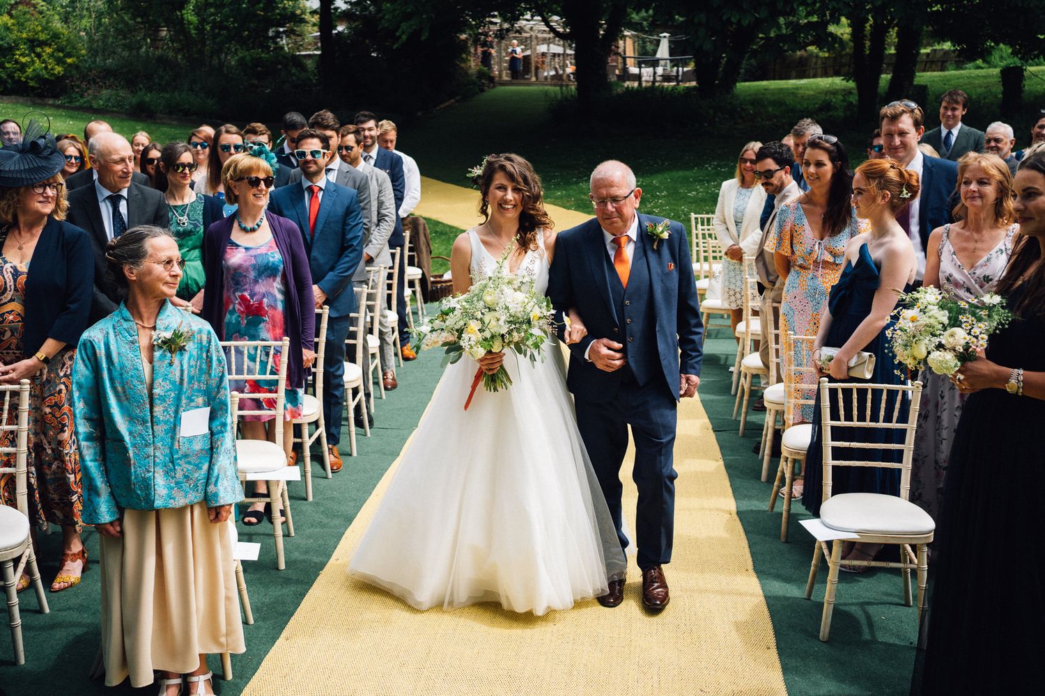 Outdoor garden wedding ceremony with white chairs arranged on manicured lawn.