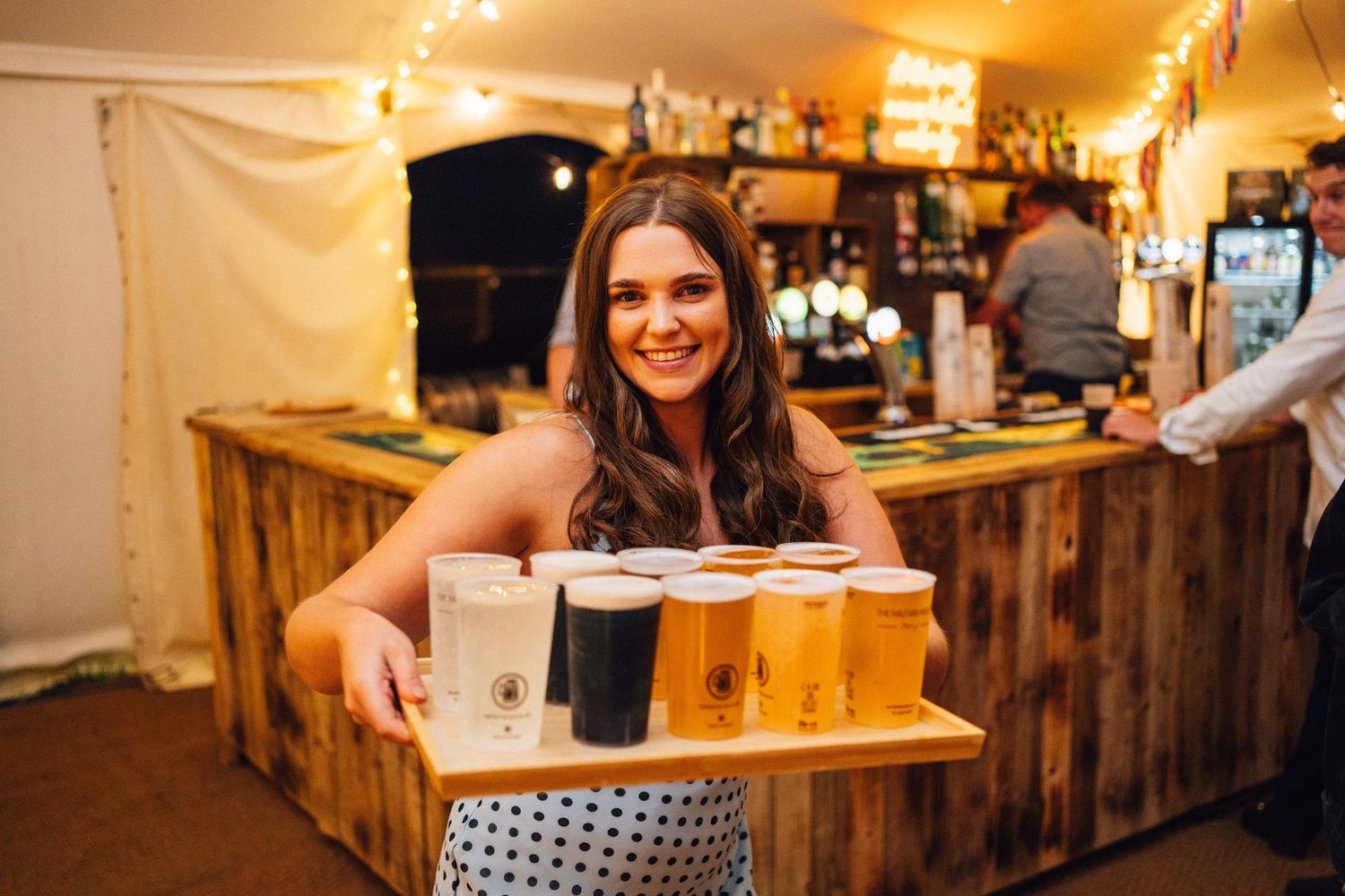 Rustic wooden bar setup with string lights creates warm ambiance at wedding reception.