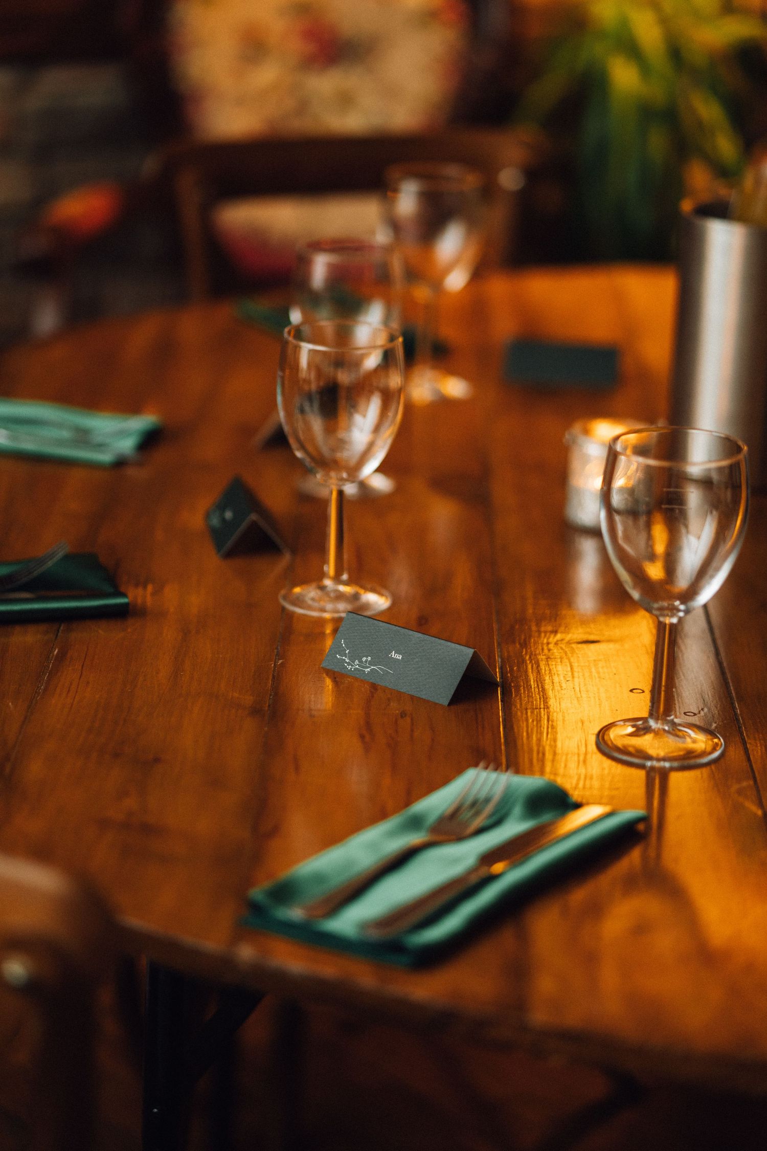 Place settings with wine glasses and turquoise napkins arranged on a rustic wooden table in warm lighting.