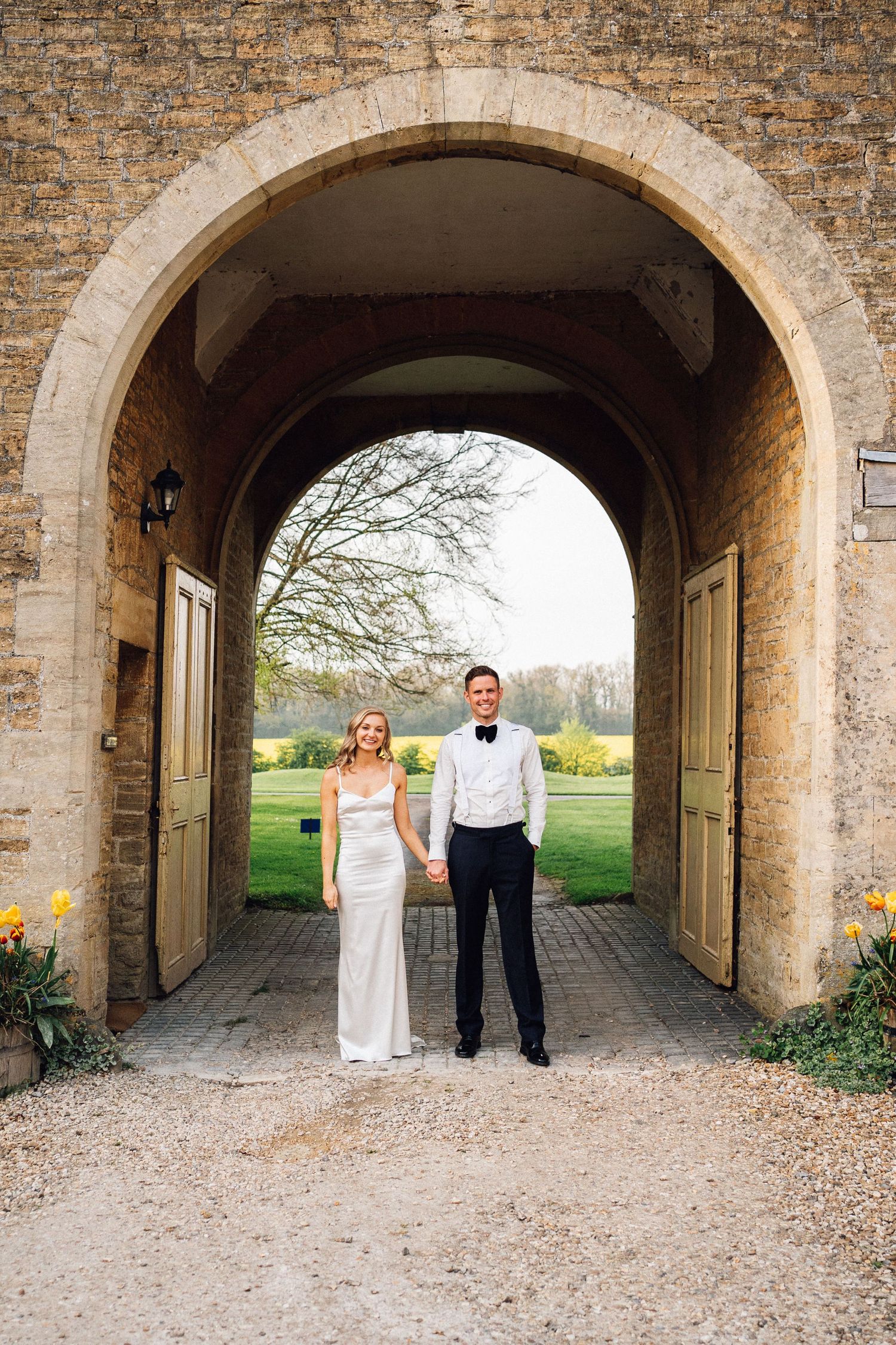 Wedding couple posing under a stone archway passage at a historic venue.
