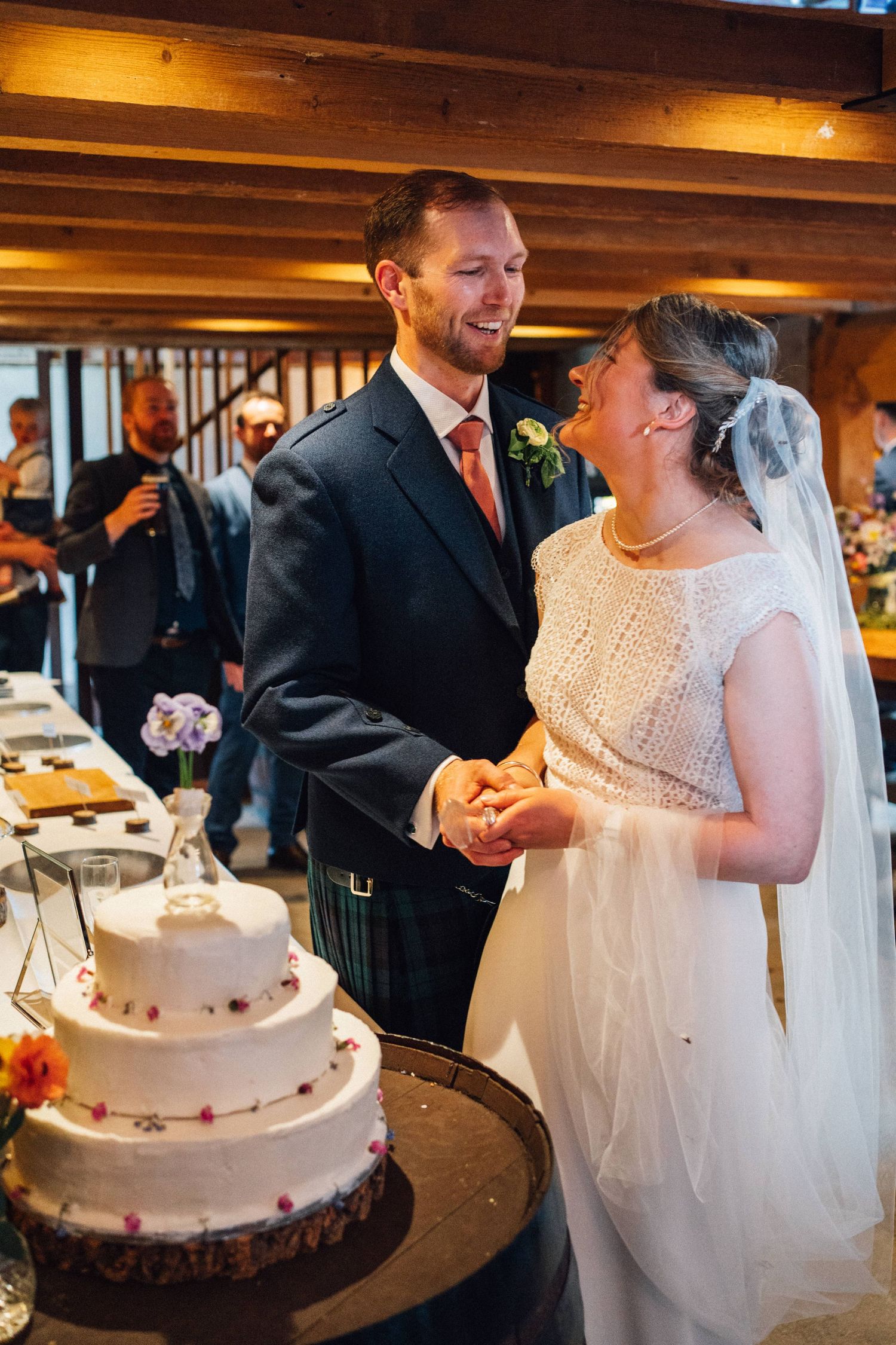 Couple shares a joyful moment while cutting their wedding cake at indoor reception.