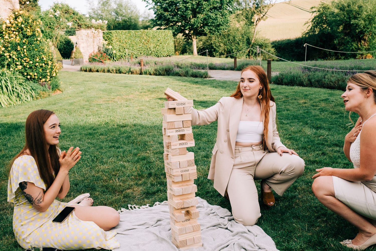 Friends playing giant Jenga game outdoors during wedding reception festivities.