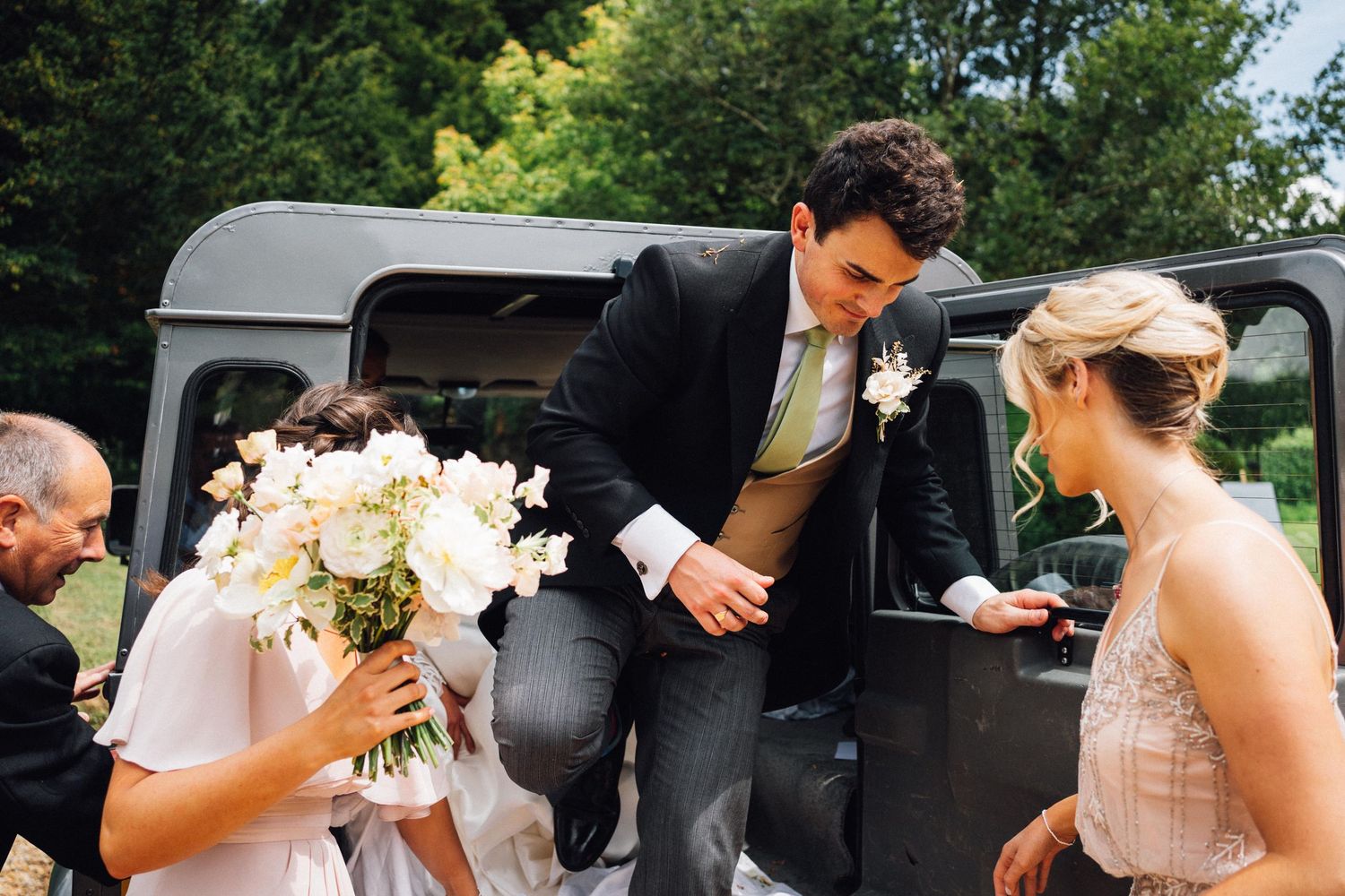 Wedding party members getting into a classic black vehicle with white bouquet.
