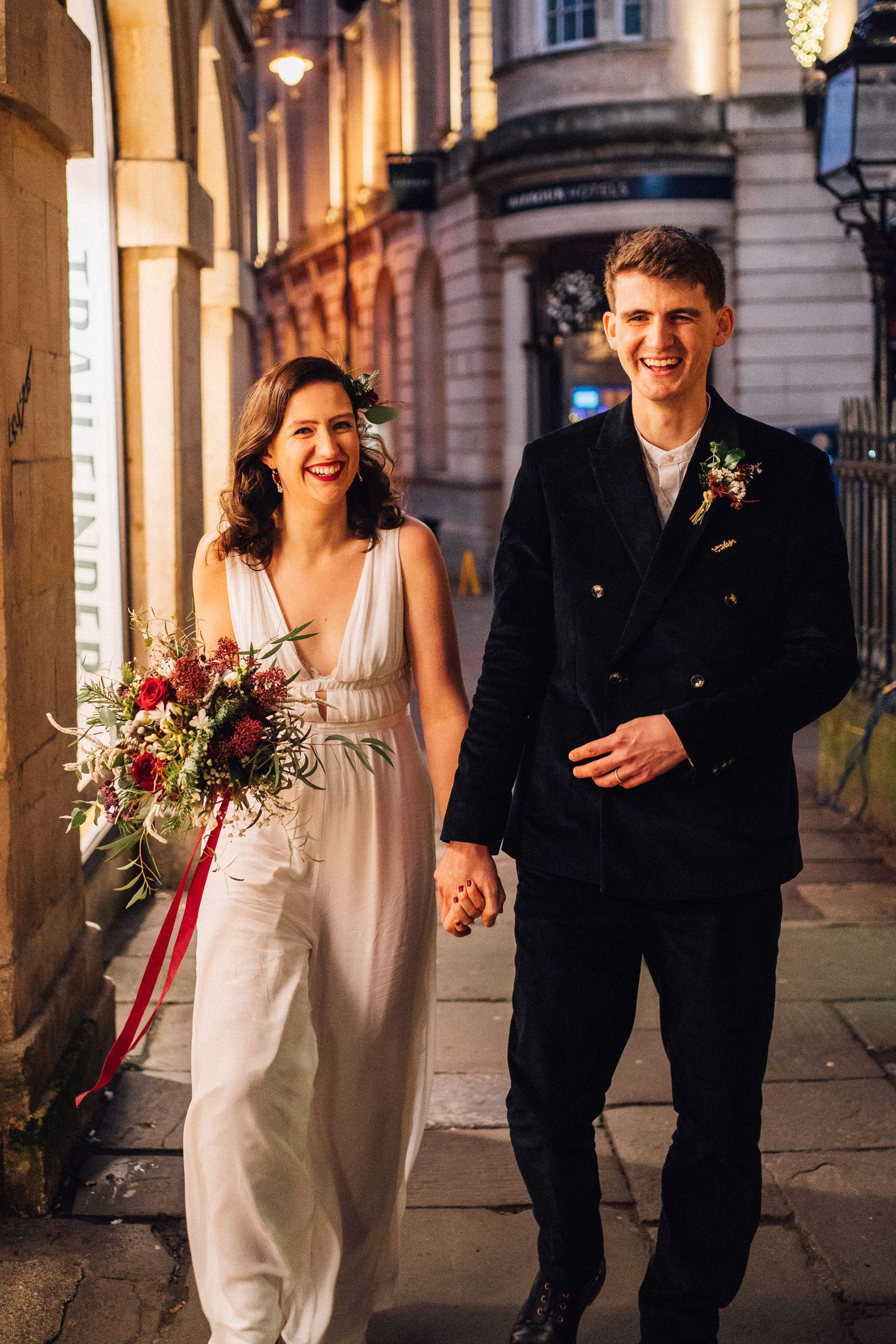 Newlyweds walking together on a city street with bride holding colorful bouquet.