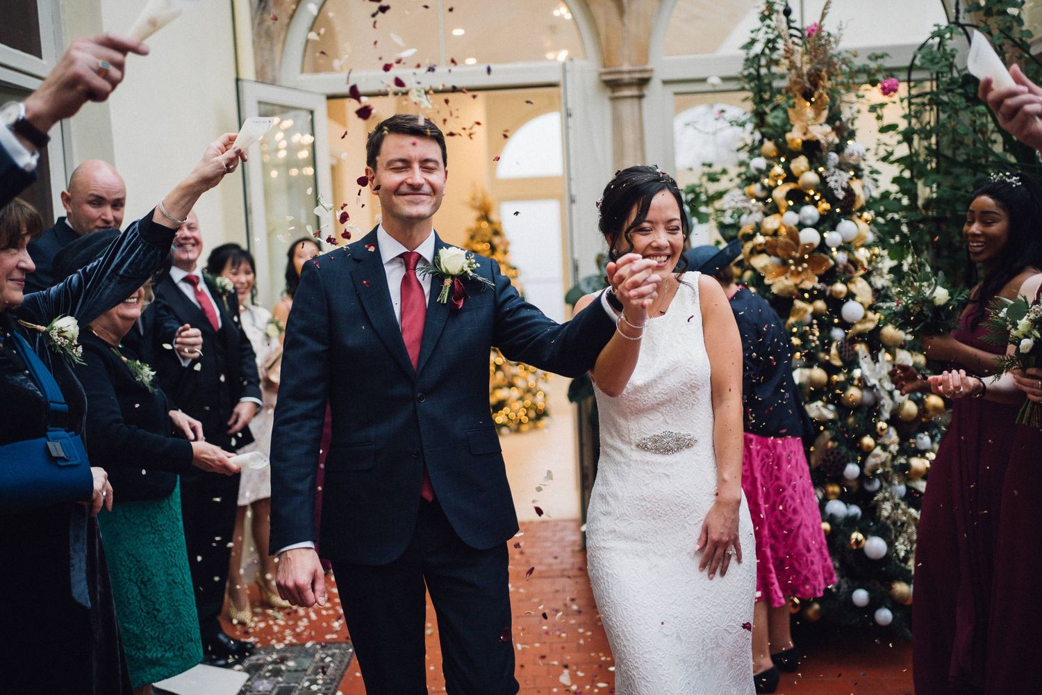 Wedding celebration with guests throwing confetti under arched walkway with floral decorations.