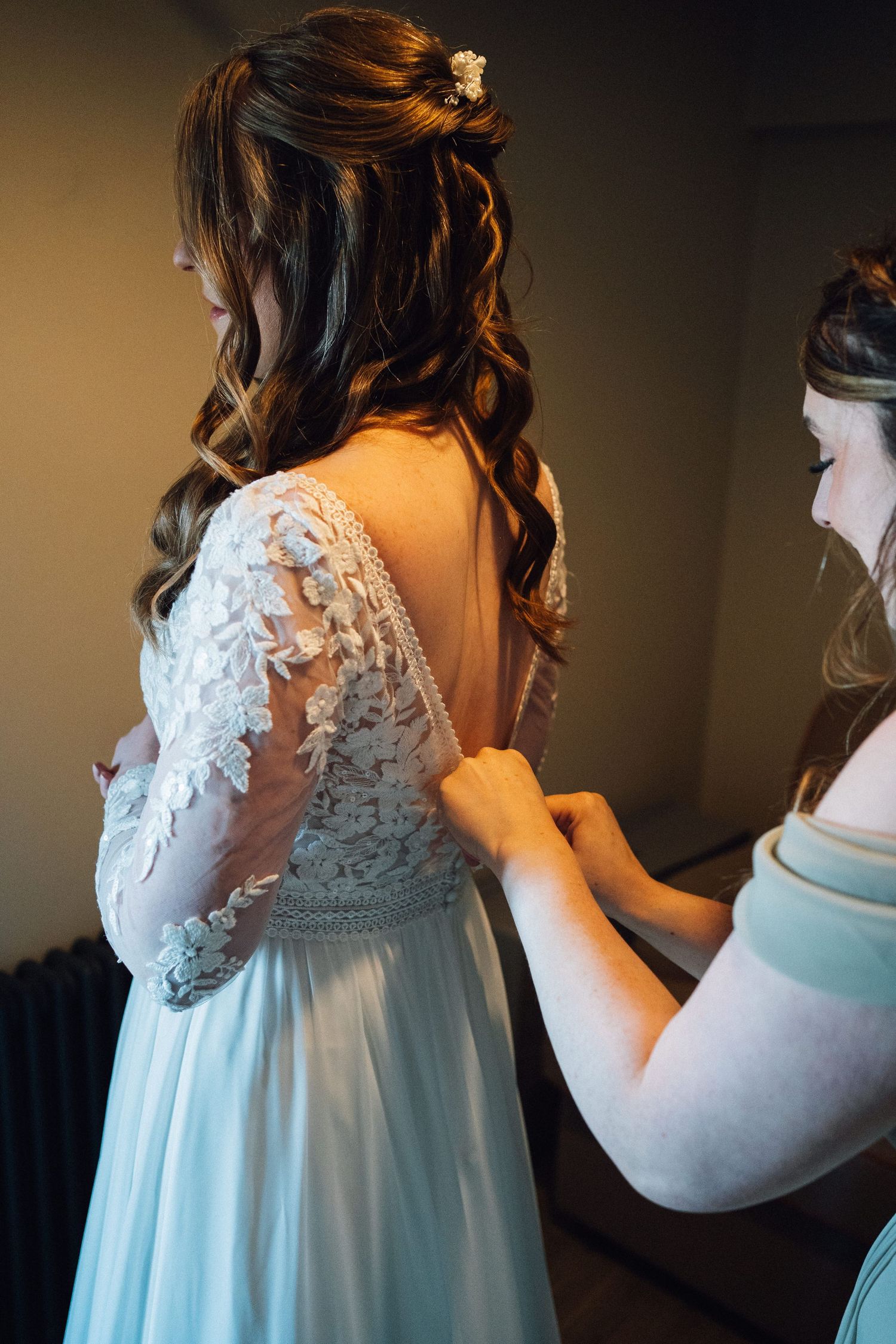 Wedding dress details showing delicate white lace appliques and sheer back design during final fitting adjustments.