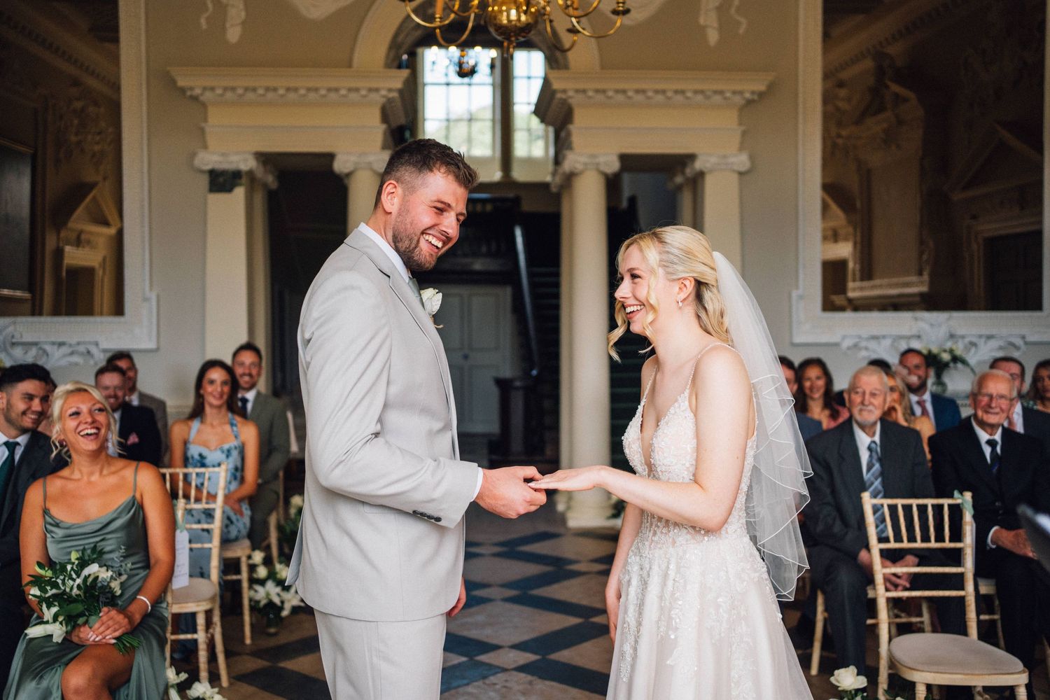 Bride and groom exchanging rings at elegant wedding ceremony with guests seated in ornate venue.