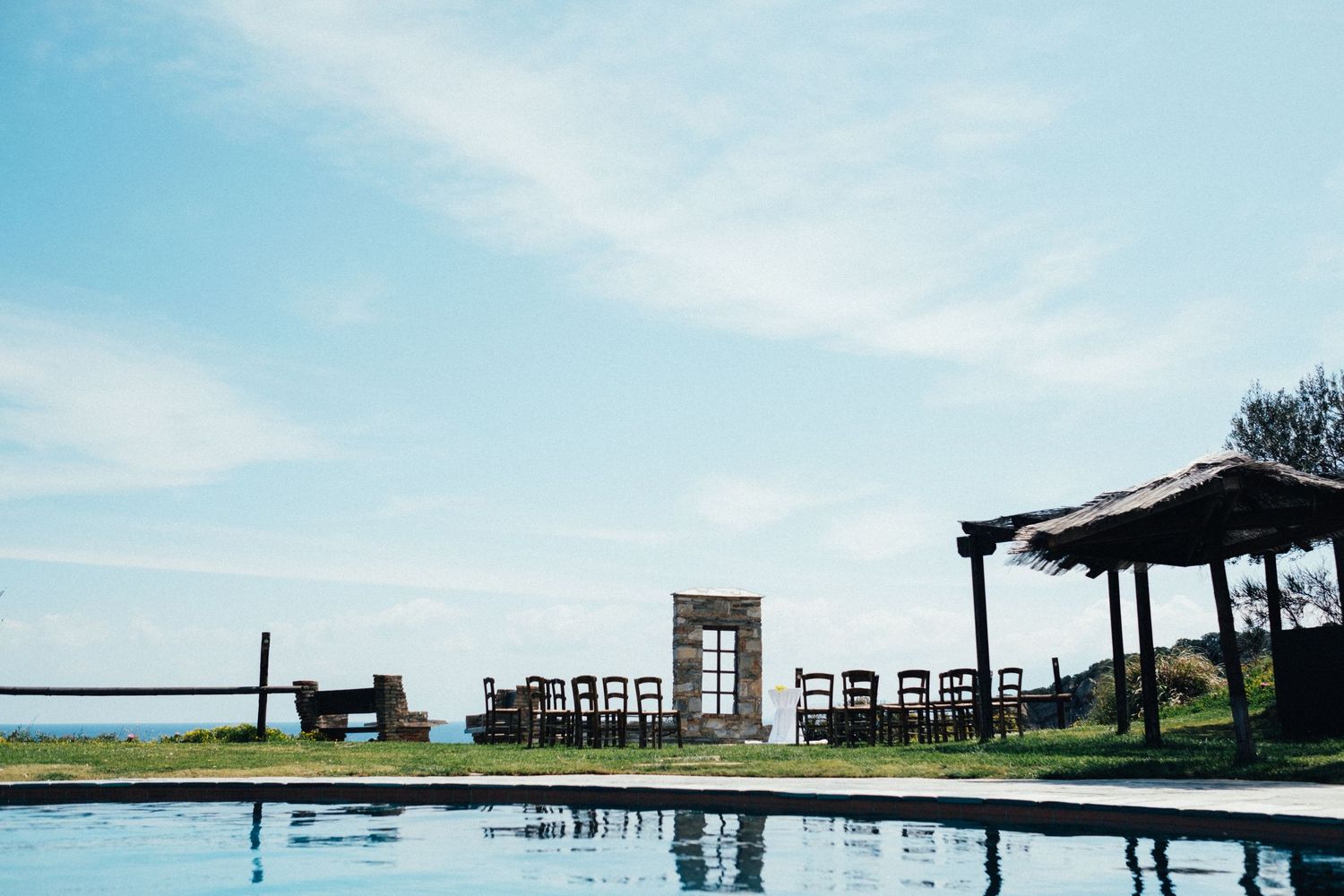 Outdoor event space with wooden pergola and seating arrangements against a bright blue sky.