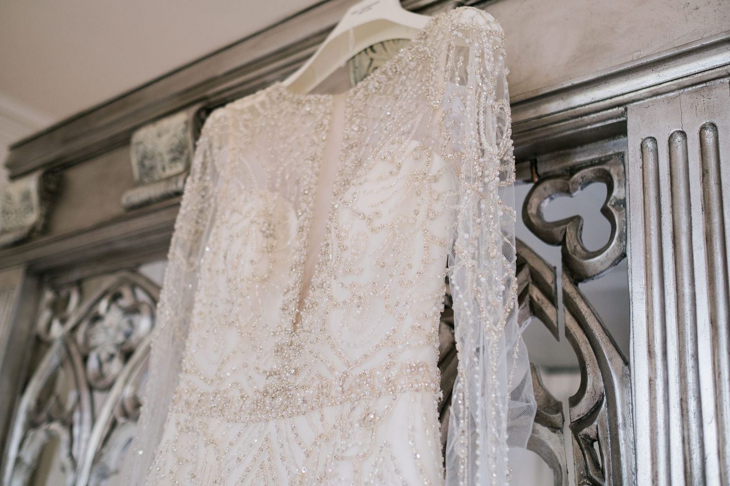 A detailed lace wedding dress hanging against an ornate carved wall.