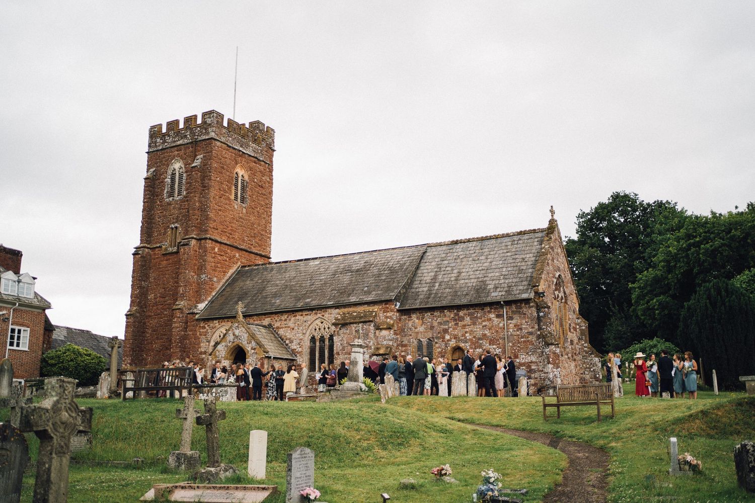 Historic brick church and cemetery grounds with wedding guests gathered outside.