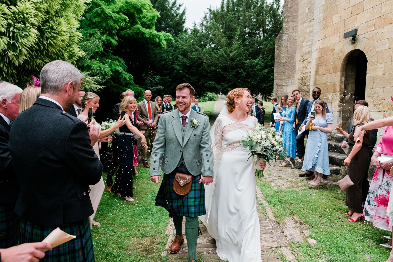 Wedding guests gather outside a historic stone church on a sunny summer day.