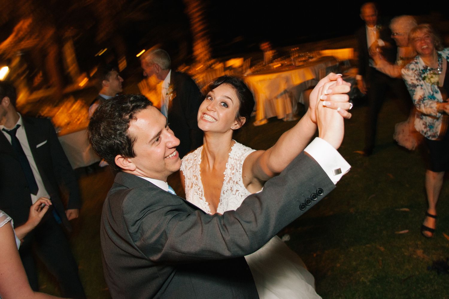 Wedding couple dancing together at their reception with guests in the background.