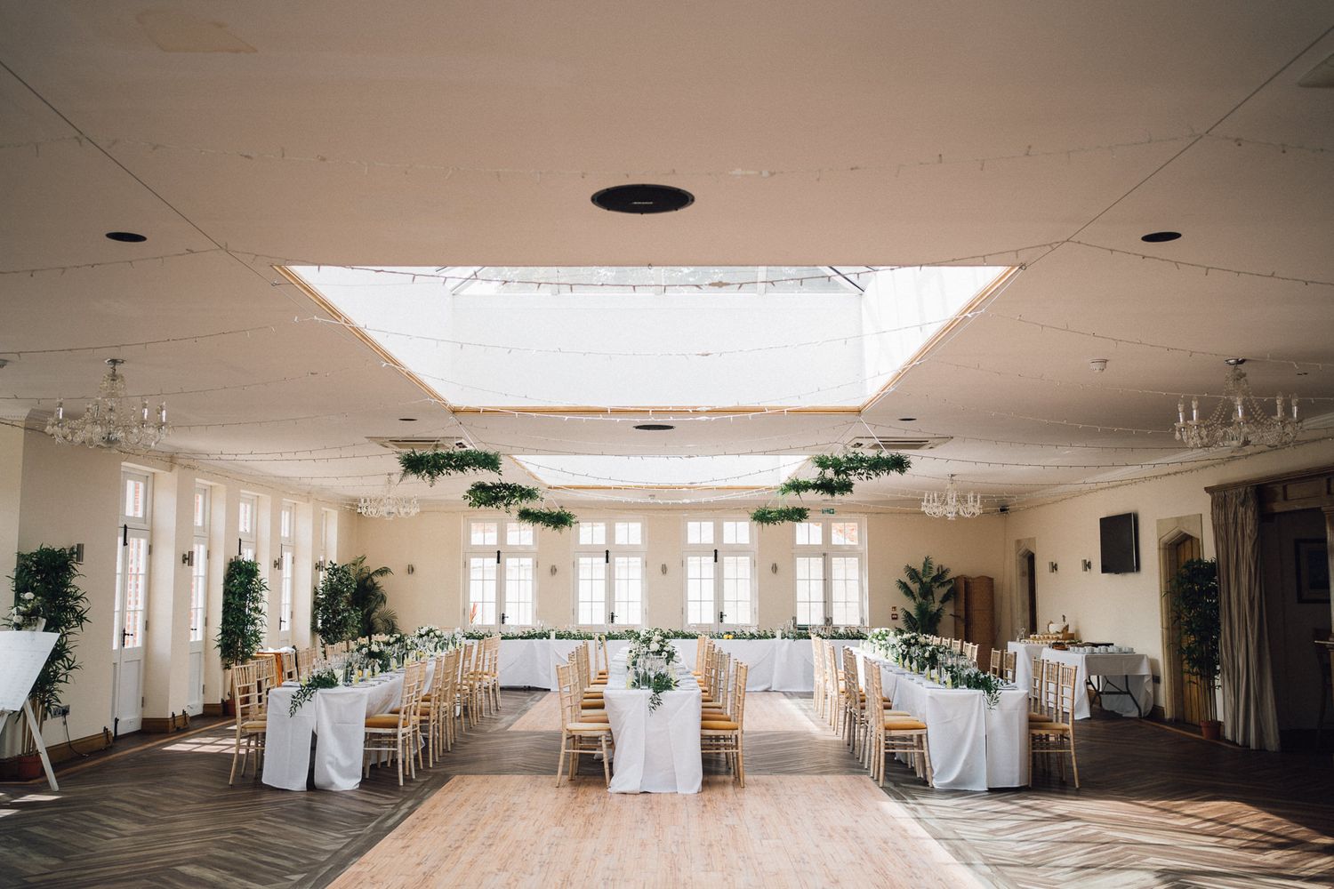 Large bright wedding reception venue with white decor and natural lighting from skylights.